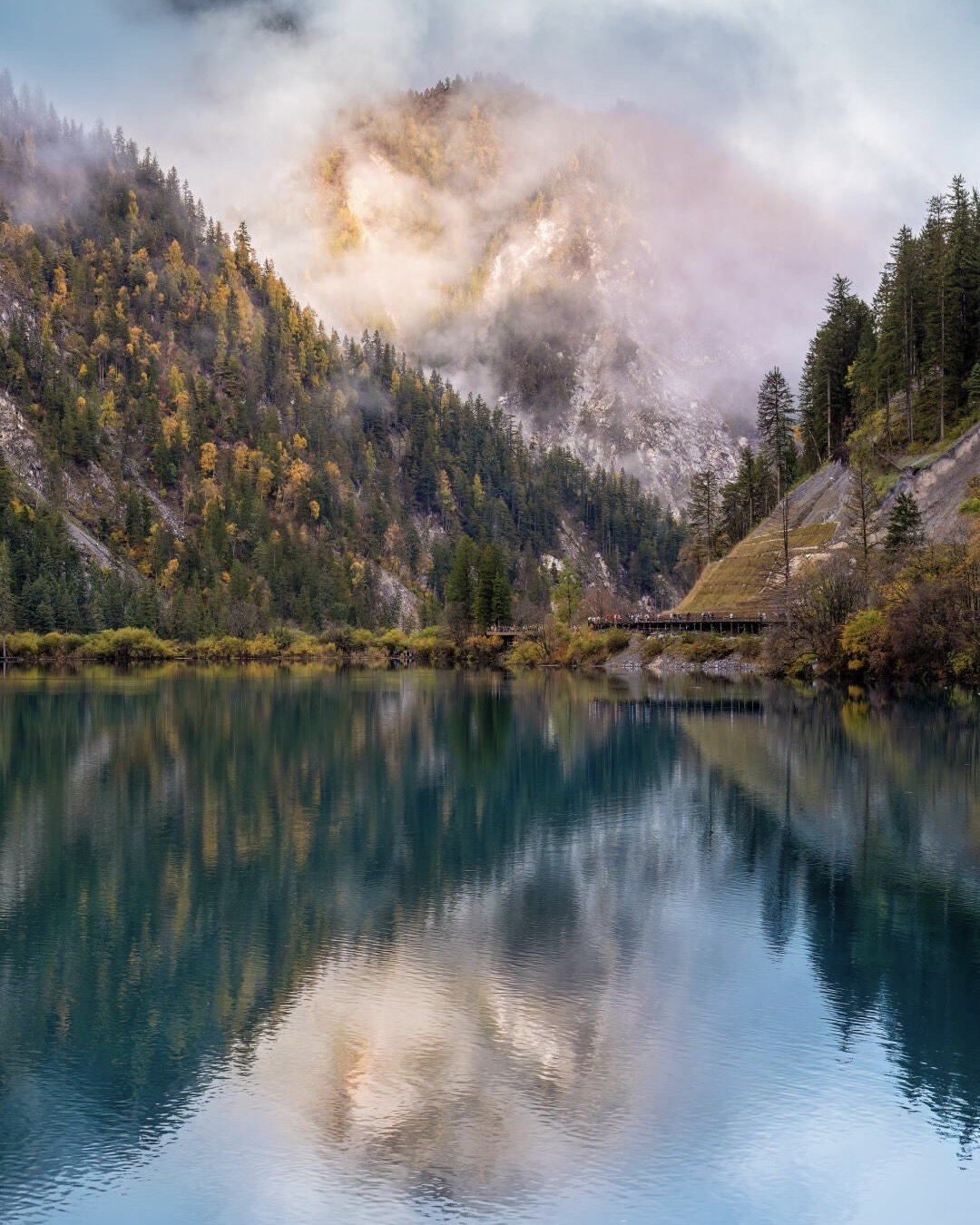 Turquoise Jiuzhaigou lake mirroring an autumn-forested peak wreathed in mist, northern Sichuan