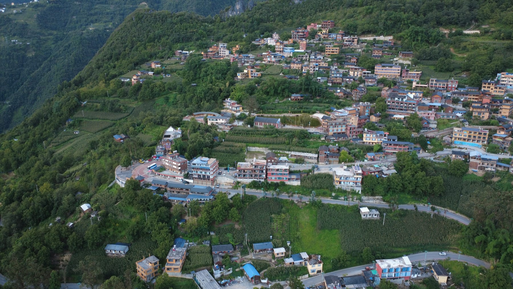 Laomudeng from the air, a village of guesthouses and houses spread along a green shelf of the Biluo range
