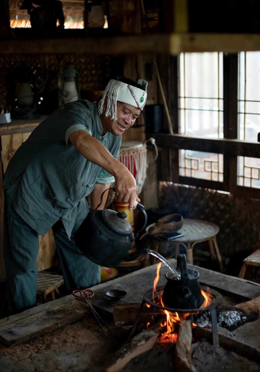 A Bulang elder pouring boiling water over fire-roasted tea leaves at the clay fire pit