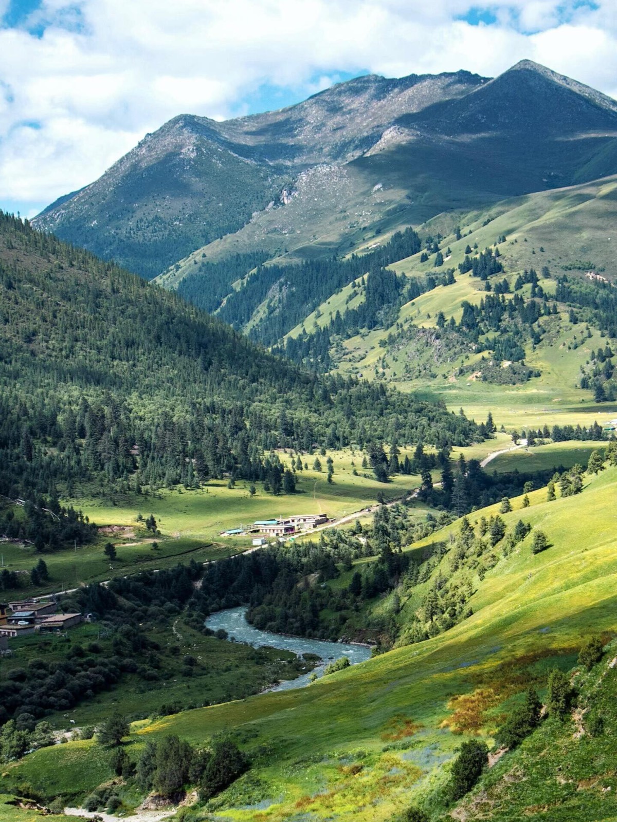 A wide-angle view of the Gani-Nie valley showing a small cluster of buildings nestled among sprawlin