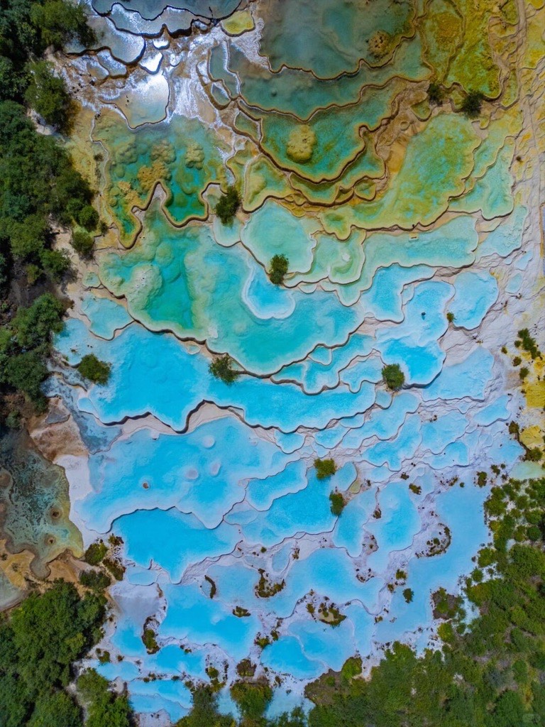 Aerial perspective of the "Five-Colored Ponds" in Huanglong, showing intricate, scalloped limestone 