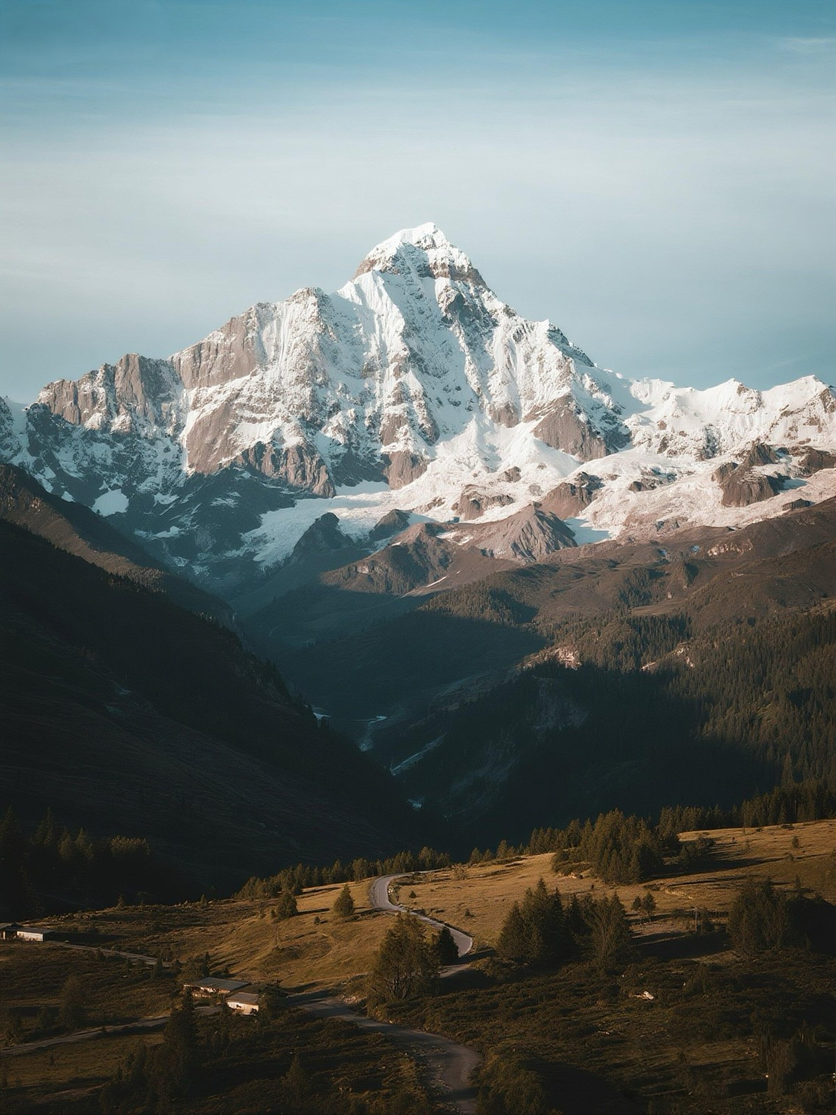 A dramatic view of a towering, snow-dusted granite mountain illuminated by sunlight, overlooking a d