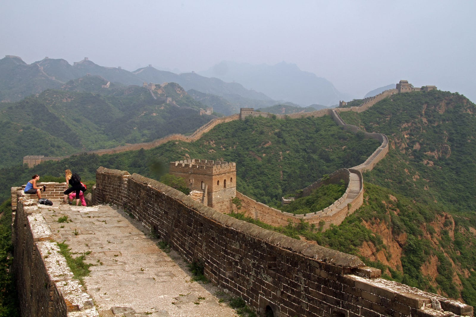 Walkers resting on top of the Great Wall on the way from Gubeikou to Jinshanling, the wall curving away over green summer ridges to distant watchtowers