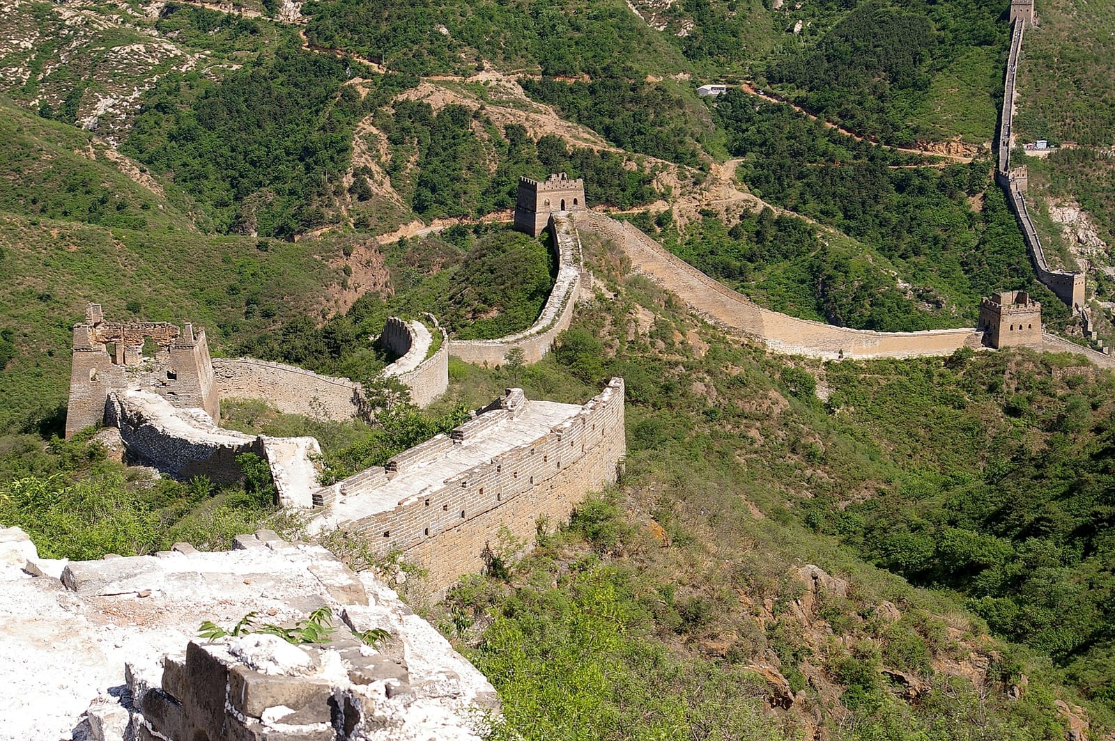 The Great Wall at Simatai winding through green scrub past a half-ruined watchtower, the ridge climbing steeply beyond