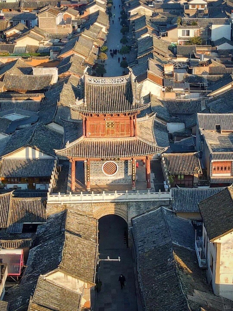 Aerial view of a historic tiered gate tower over grey-tiled old-town rooftops in West Yunnan