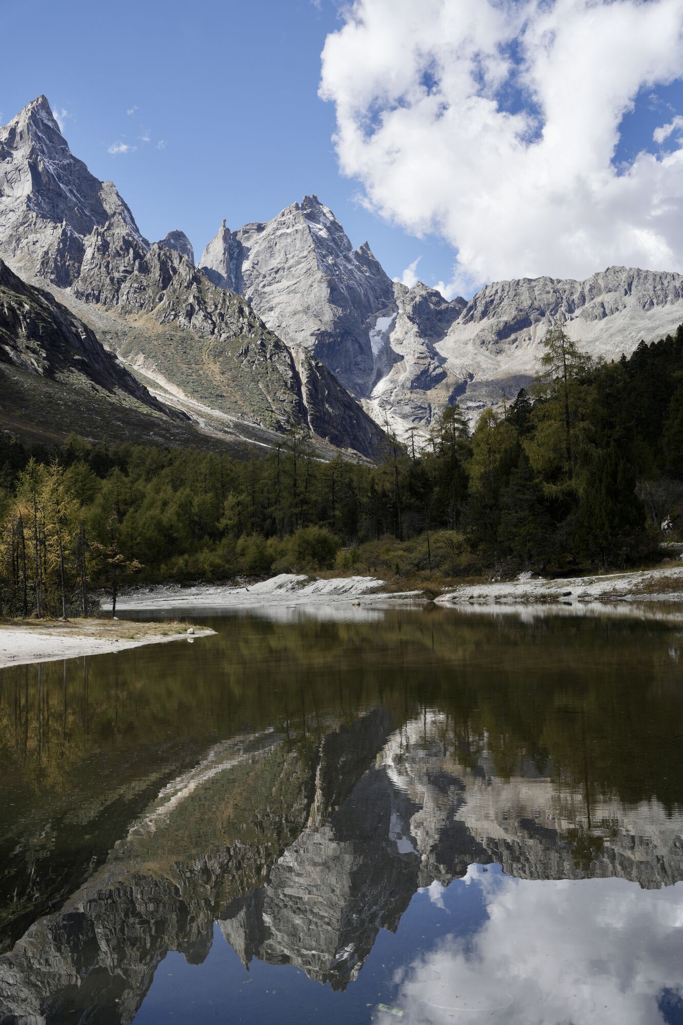 Razor-sharp twin peaks mirrored in a still alpine tarn with autumn larch on the shore