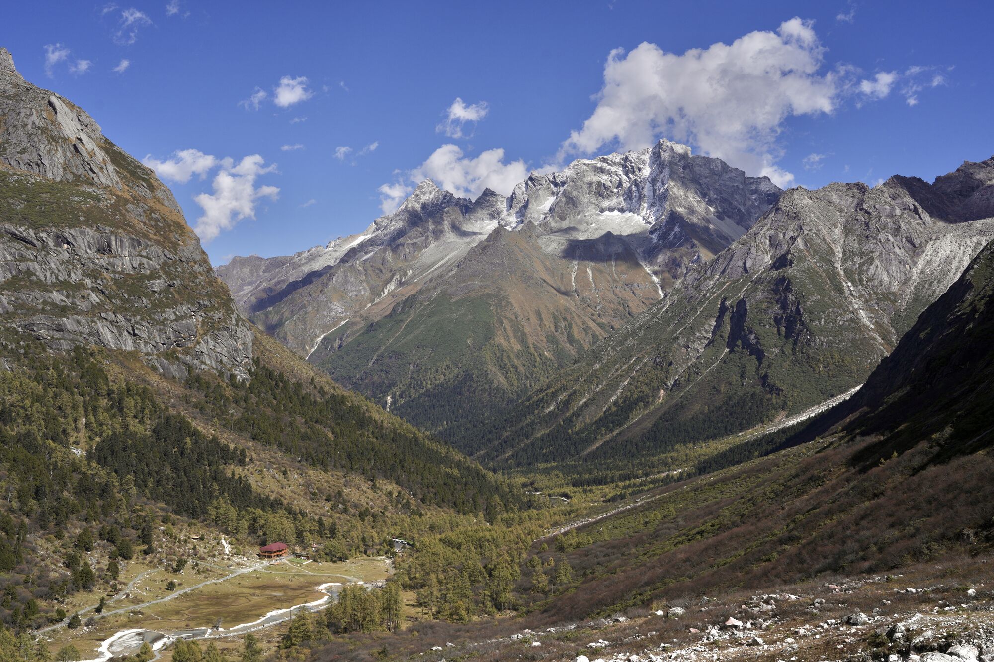 Grand V-shaped glacial valley panorama in Bipeng, red-roofed lodge beside a winding stream