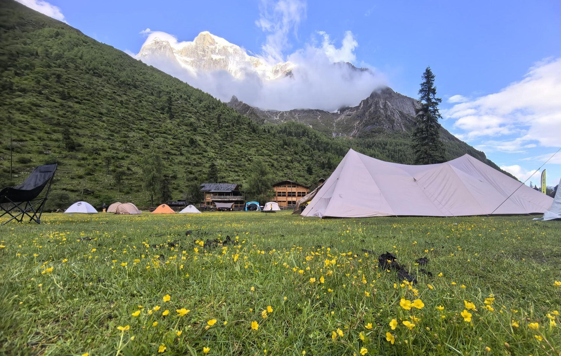 Cream canvas tents pitched in a buttercup meadow below a snow peak — trek camp at Muzuozi