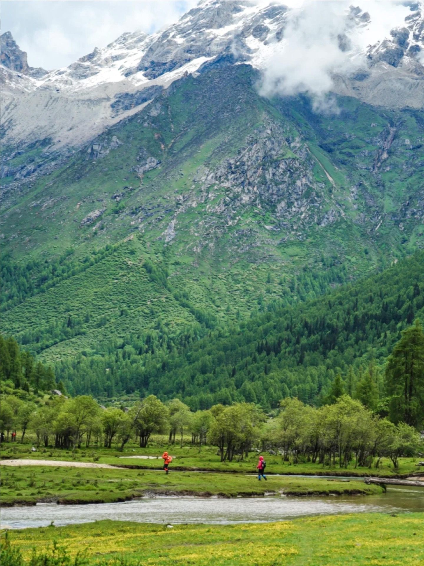 Two trekkers in red against the vast green wall of Changping Valley — scale shot at the trailhead