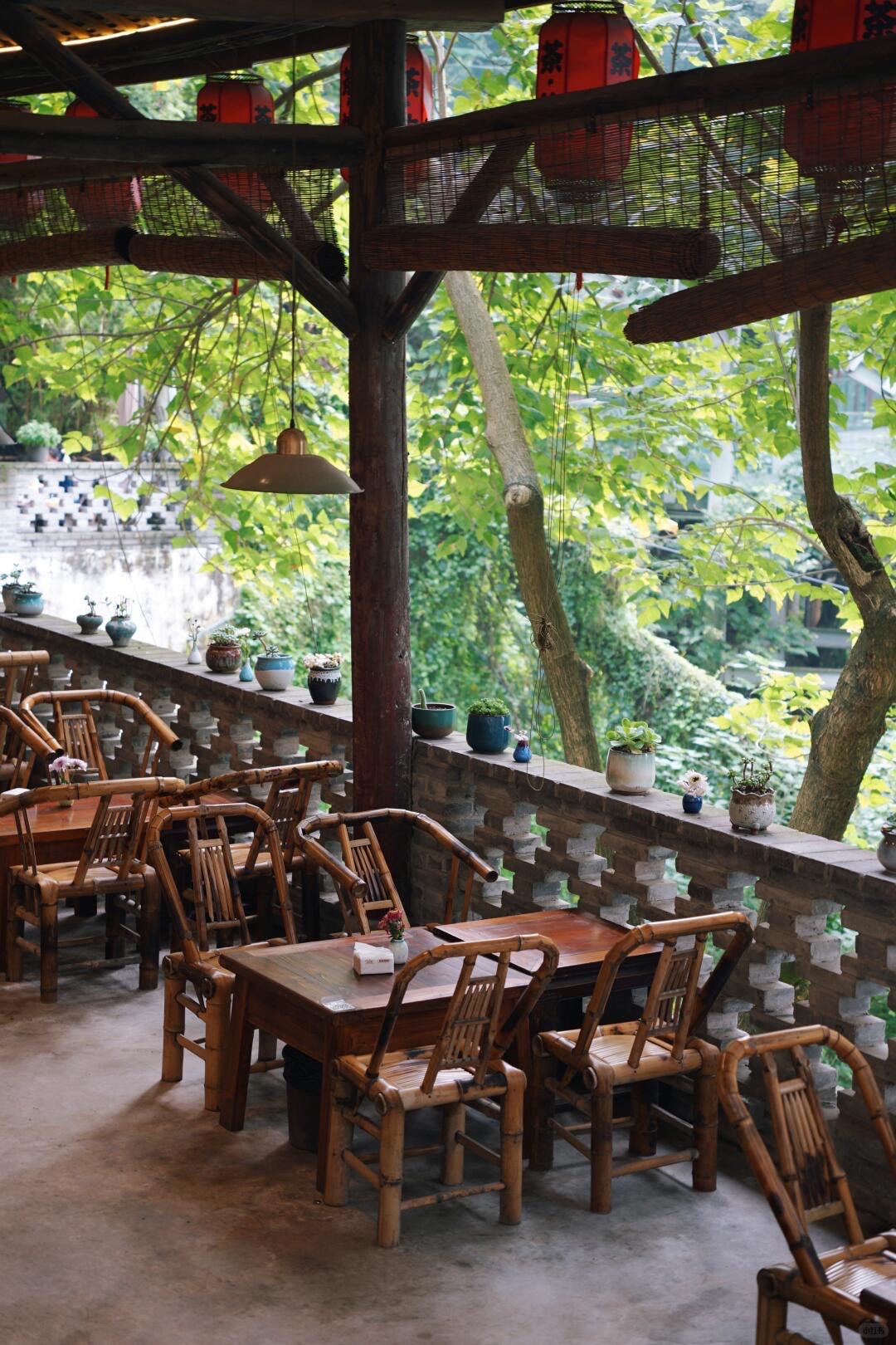 Traditional teahouse terrace with bamboo chairs, red lanterns and potted plants amid greenery in Chongqing.