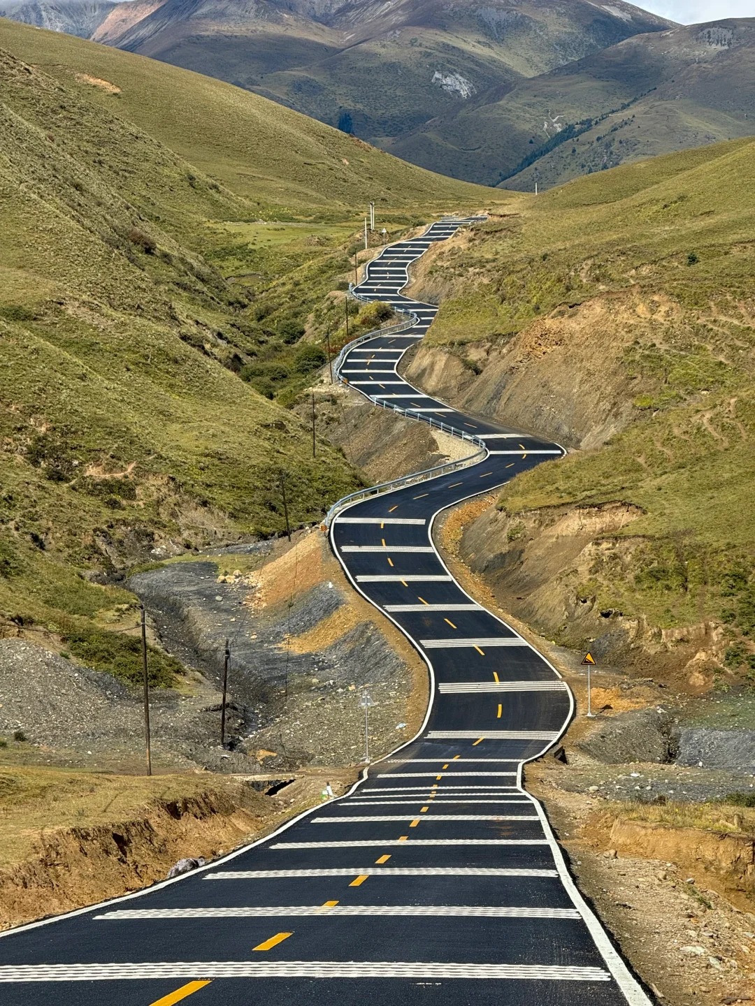 Ribboned blacktop winding through emerald grass hills near Zhangna, the Genie south route
