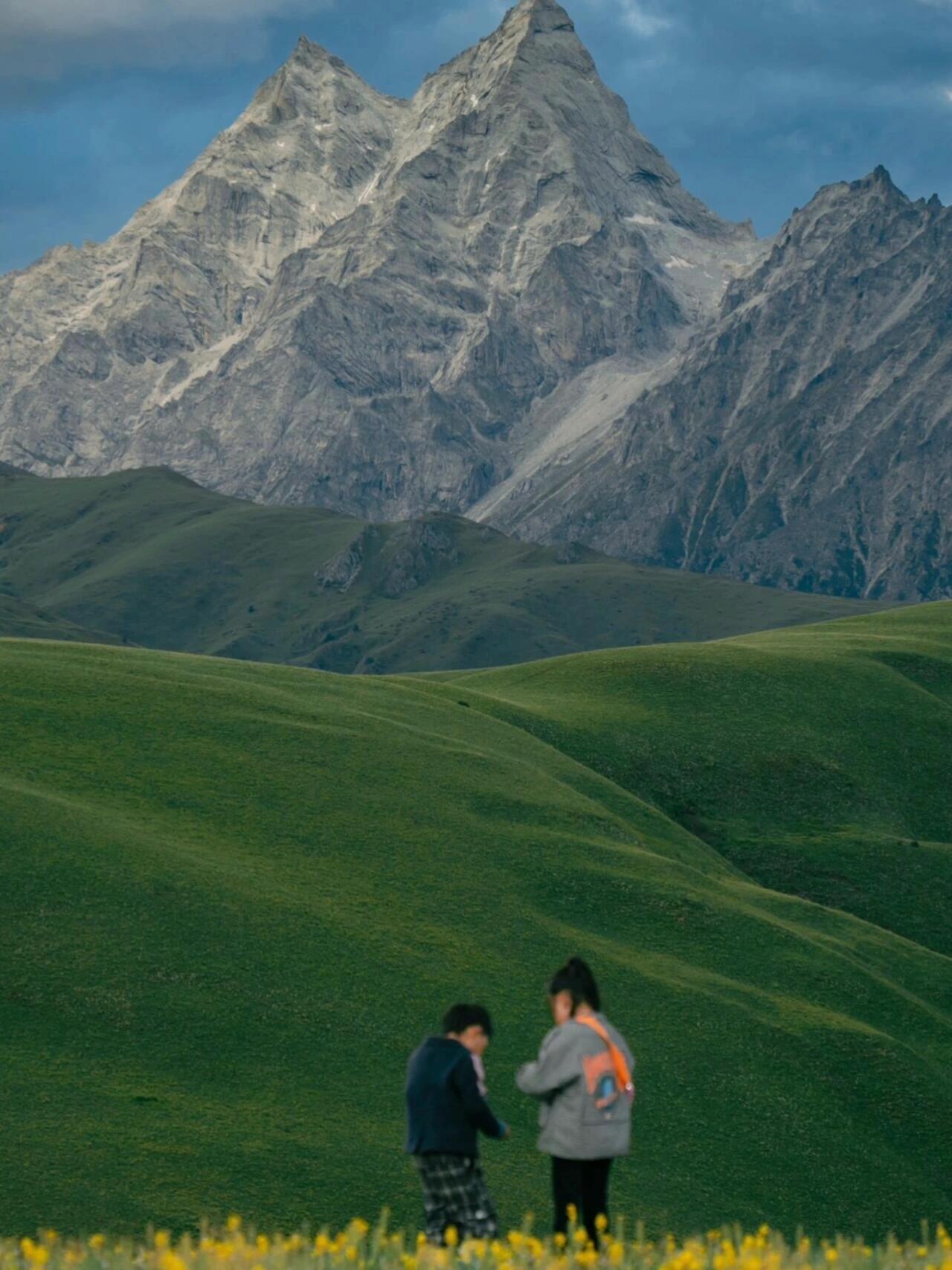 Trekkers paused in an alpine meadow — tiny figures against the enormous snow wall