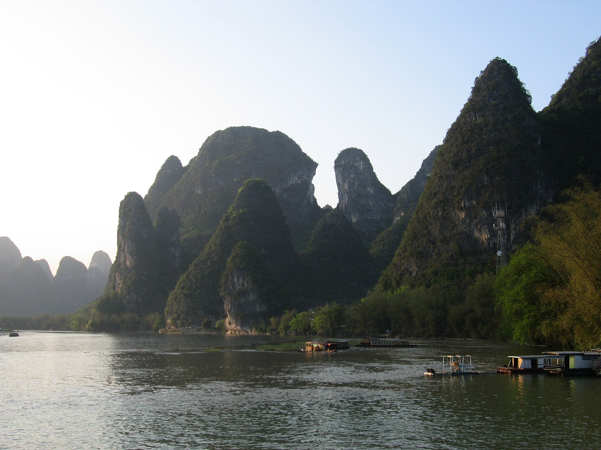 Towering karst peaks rising above the Li River (漓江) in golden afternoon light, bamboo rafts drifting below, Guilin