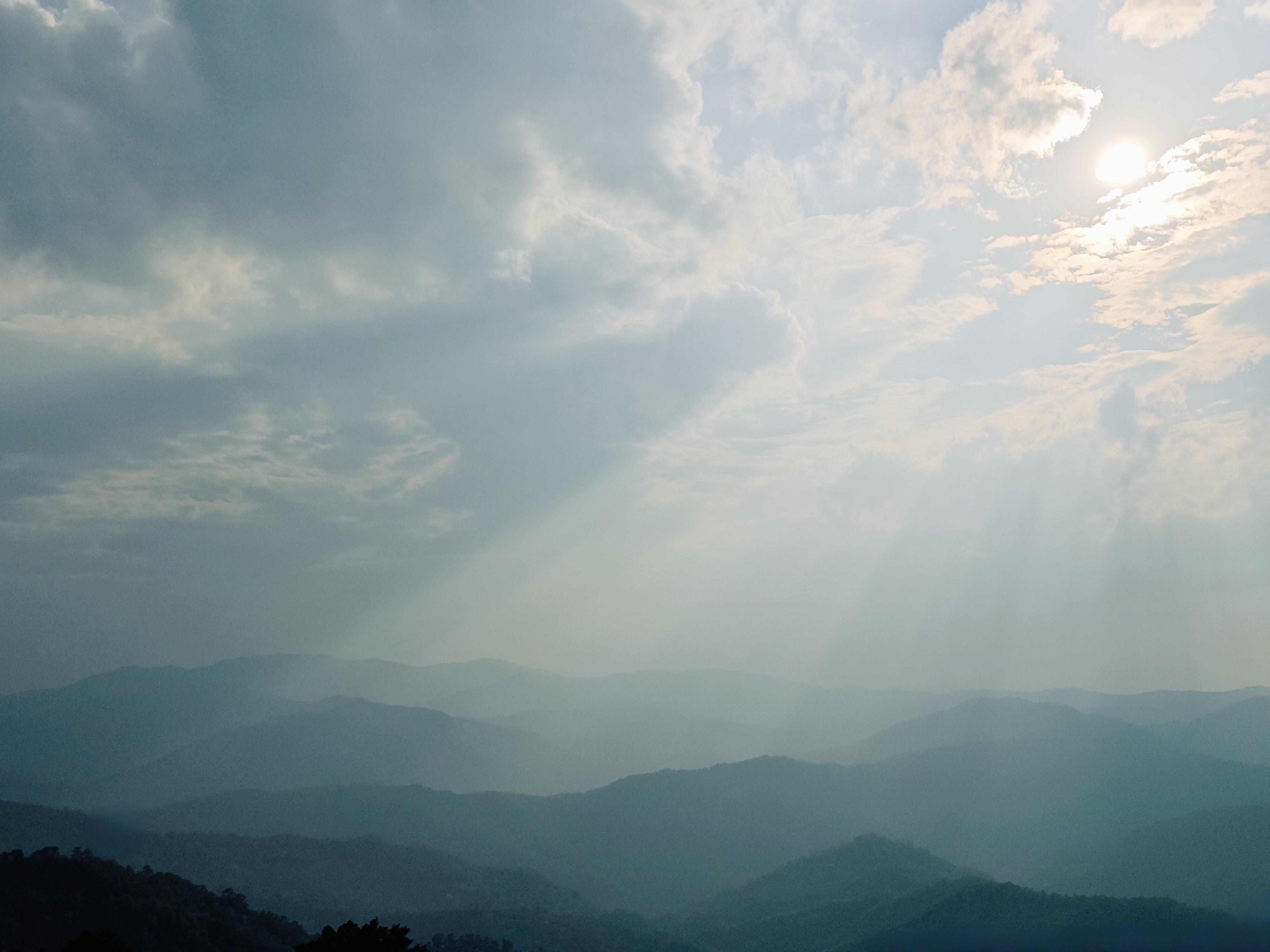 Sun rays through clouds over the layered Jingmai mountain ridges