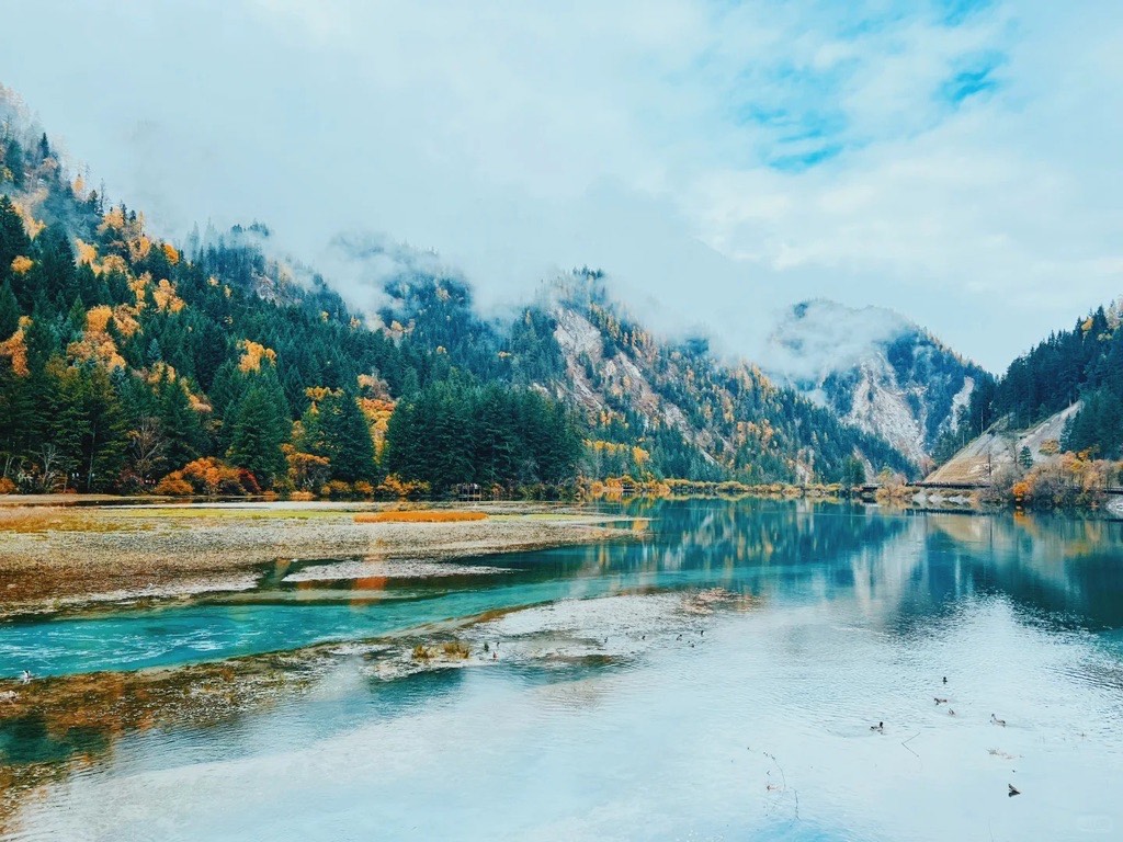 Wide Jiuzhai Valley lake in autumn with mist rolling off the mountains, golden larches and the valley boardwalk