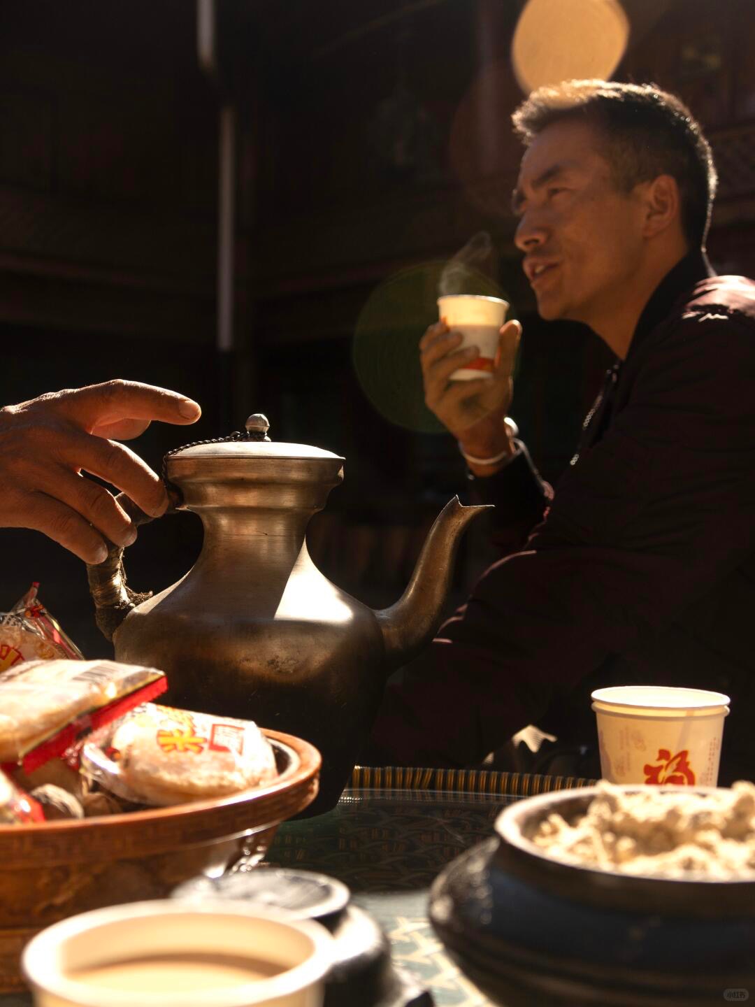 A Mosuo man drinks butter tea from a copper pot in a Lugu Lake household — matrilineal society interior