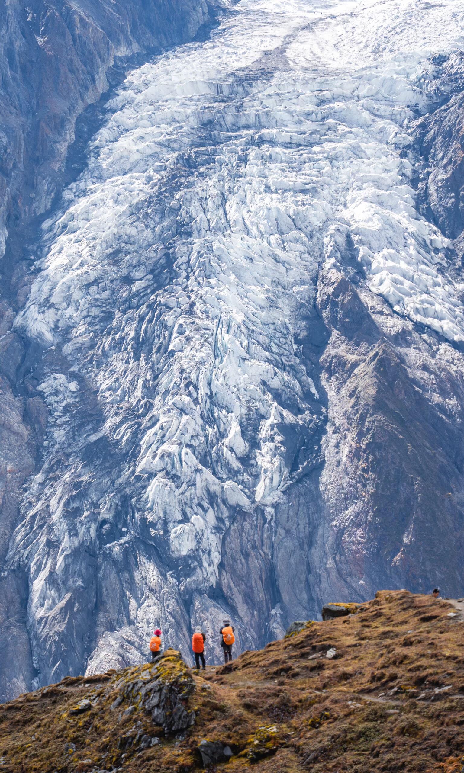 Trekkers dwarfed by a massive glacier wall — the raw scale of Meili's north face