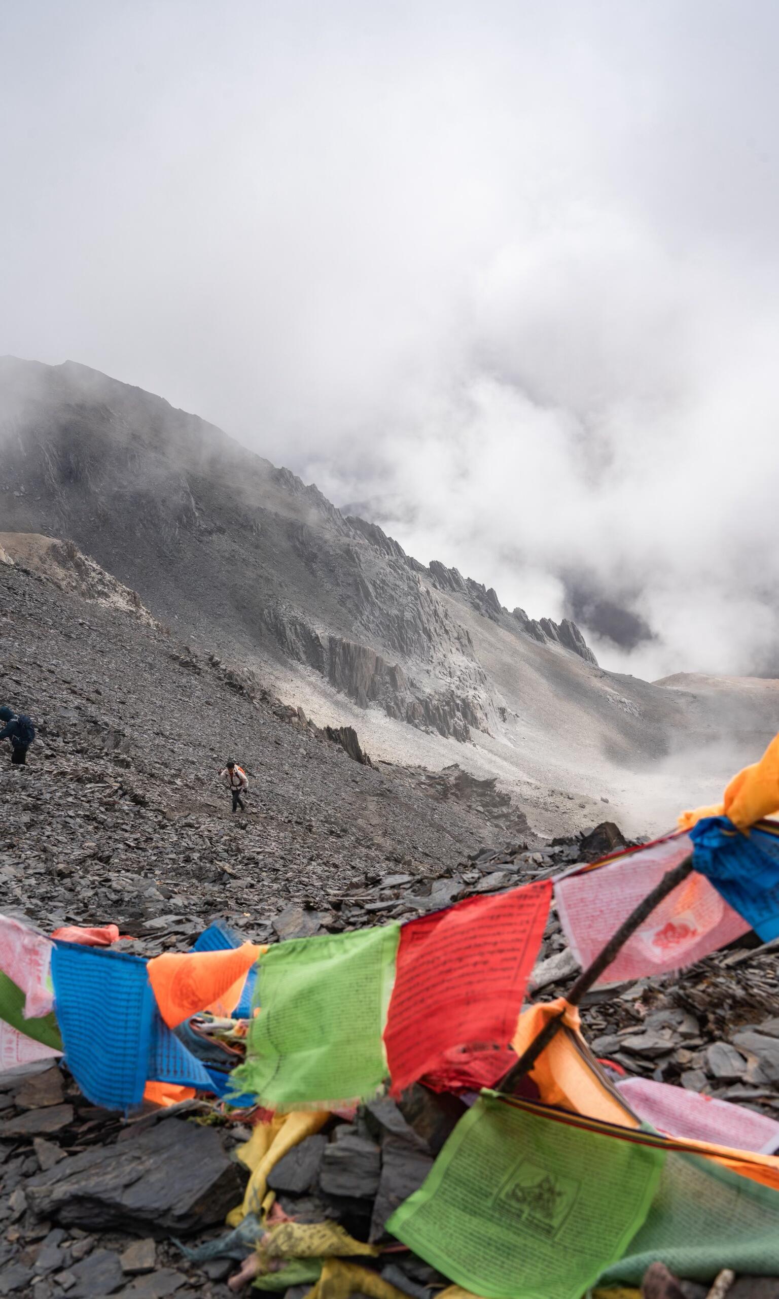 Tibetan prayer flags at a misty pass on the Meili North Slope trek — the kora atmosphere