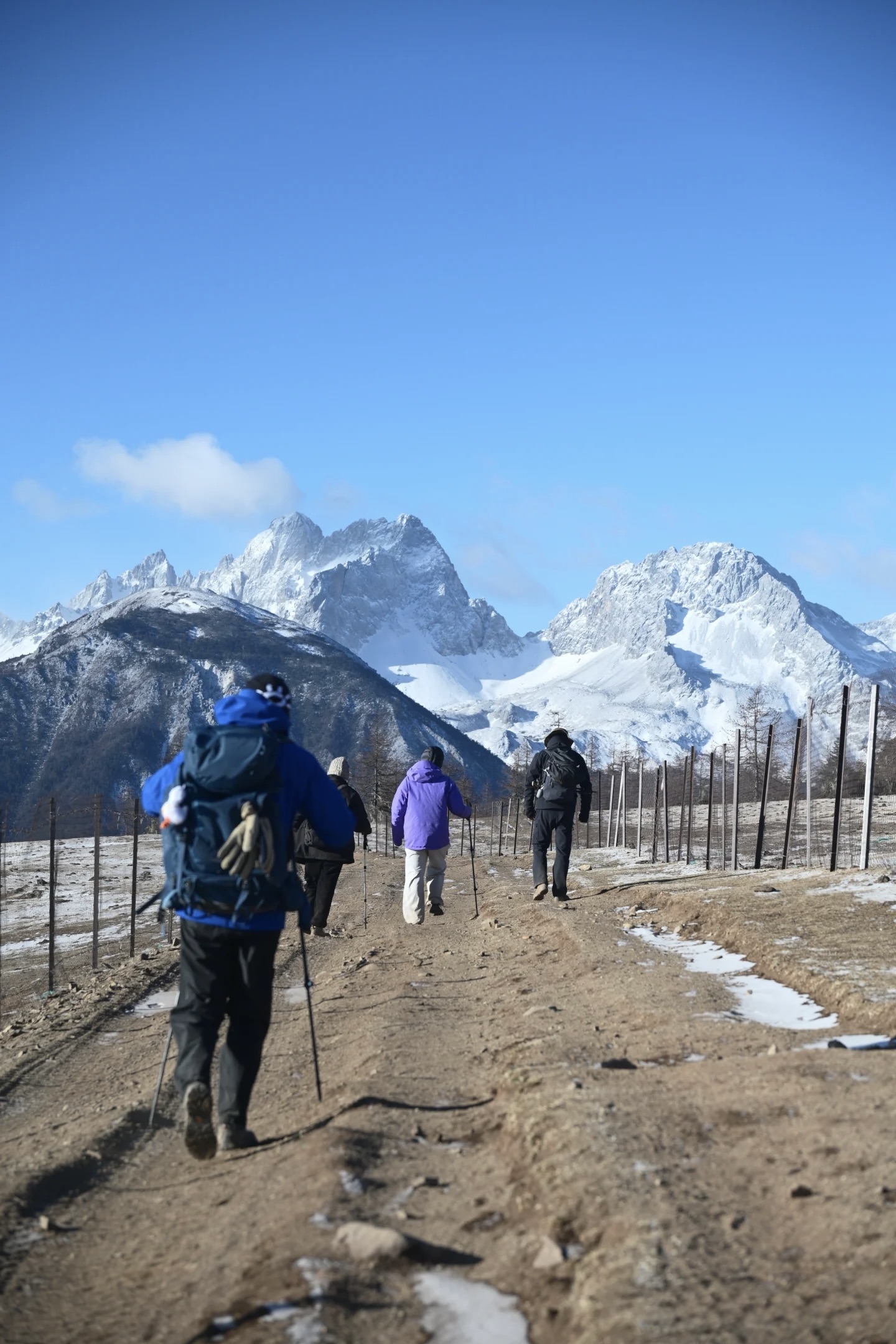 Group of trekkers in cold-weather kit walking toward the jagged Meili snow peaks — departure-morning shot