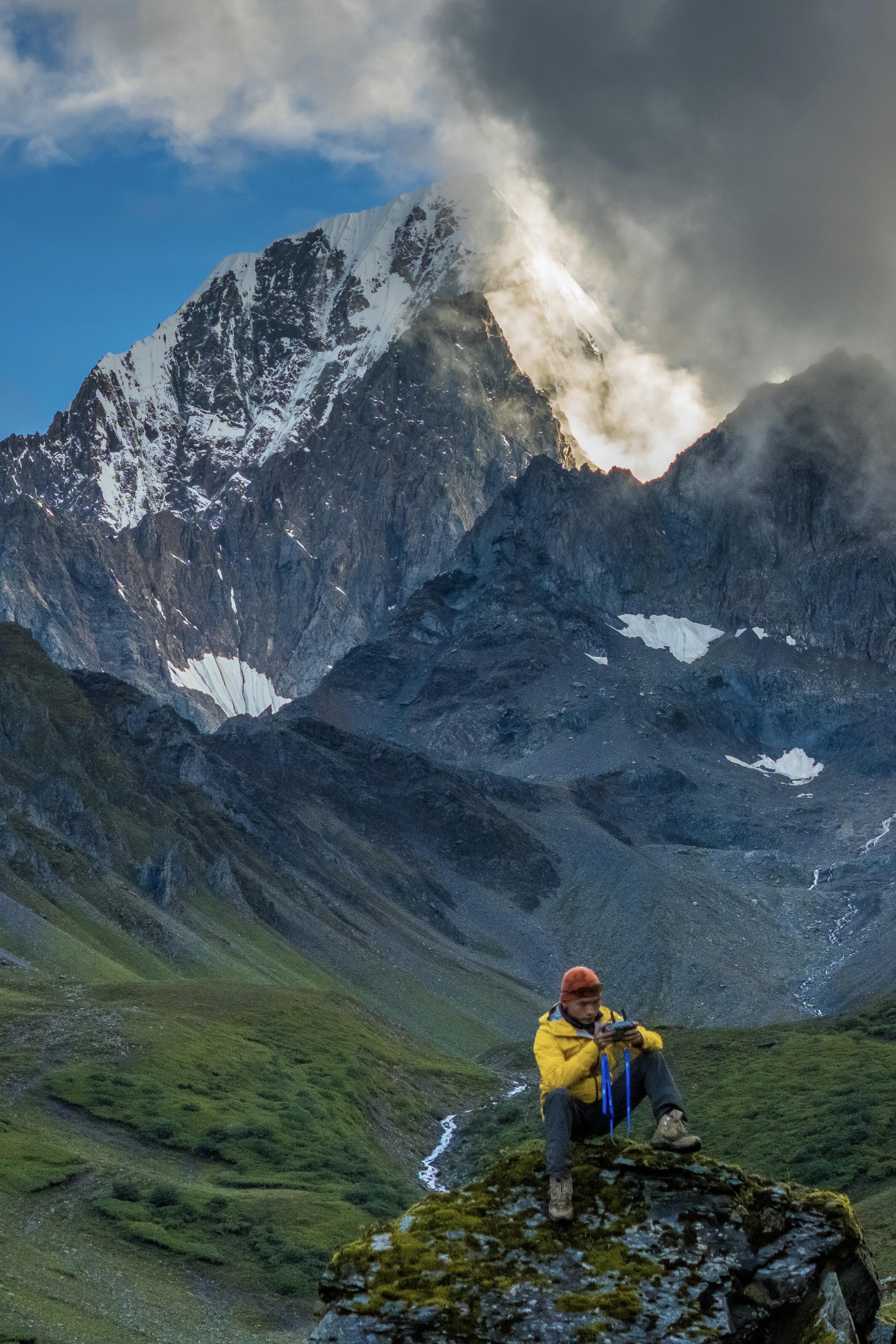 Trekker resting on a rock with a massive cloud-wrapped peak behind — the 'earned this view' moment