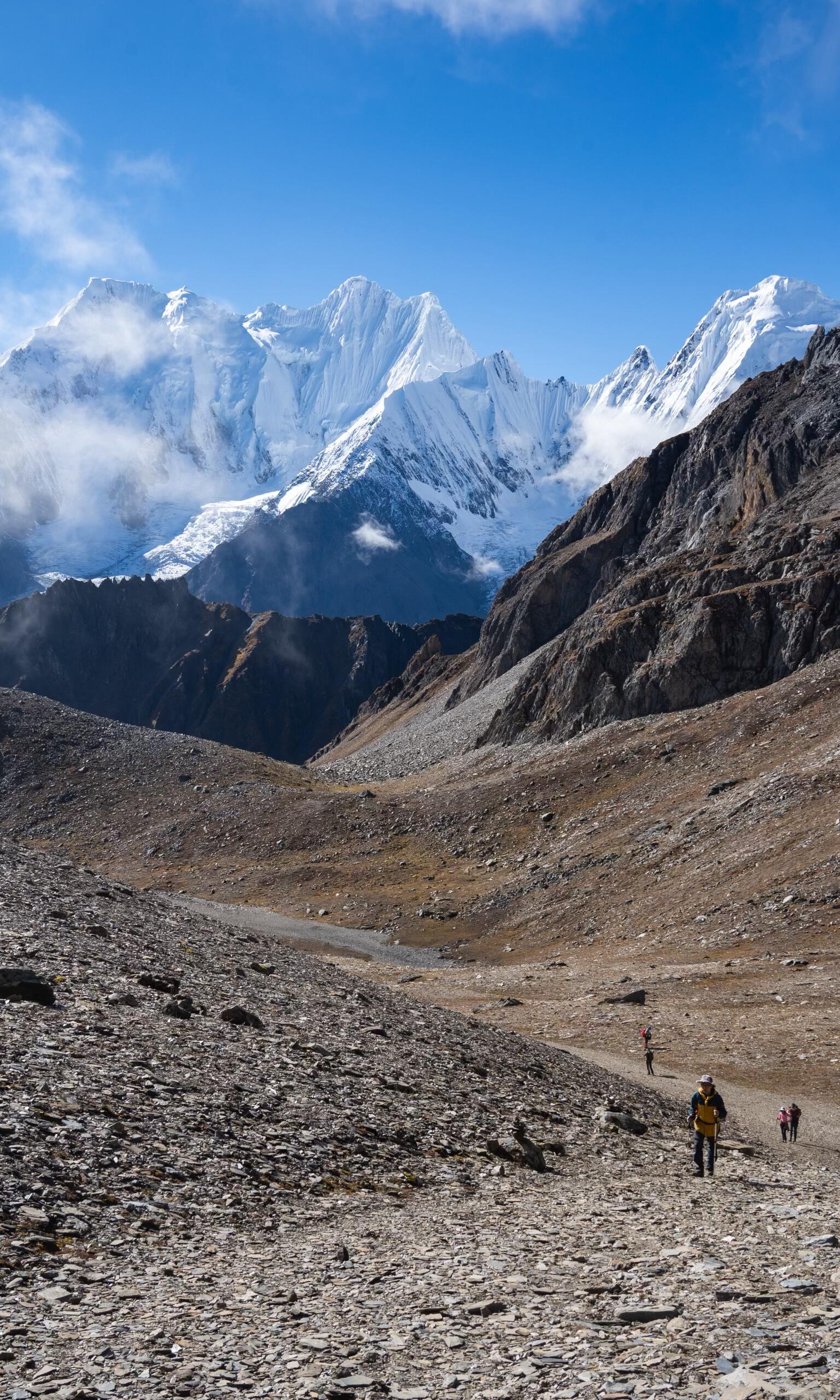 Trekkers crossing rocky terrain toward the snow peaks — high-altitude moonscape on Day 5