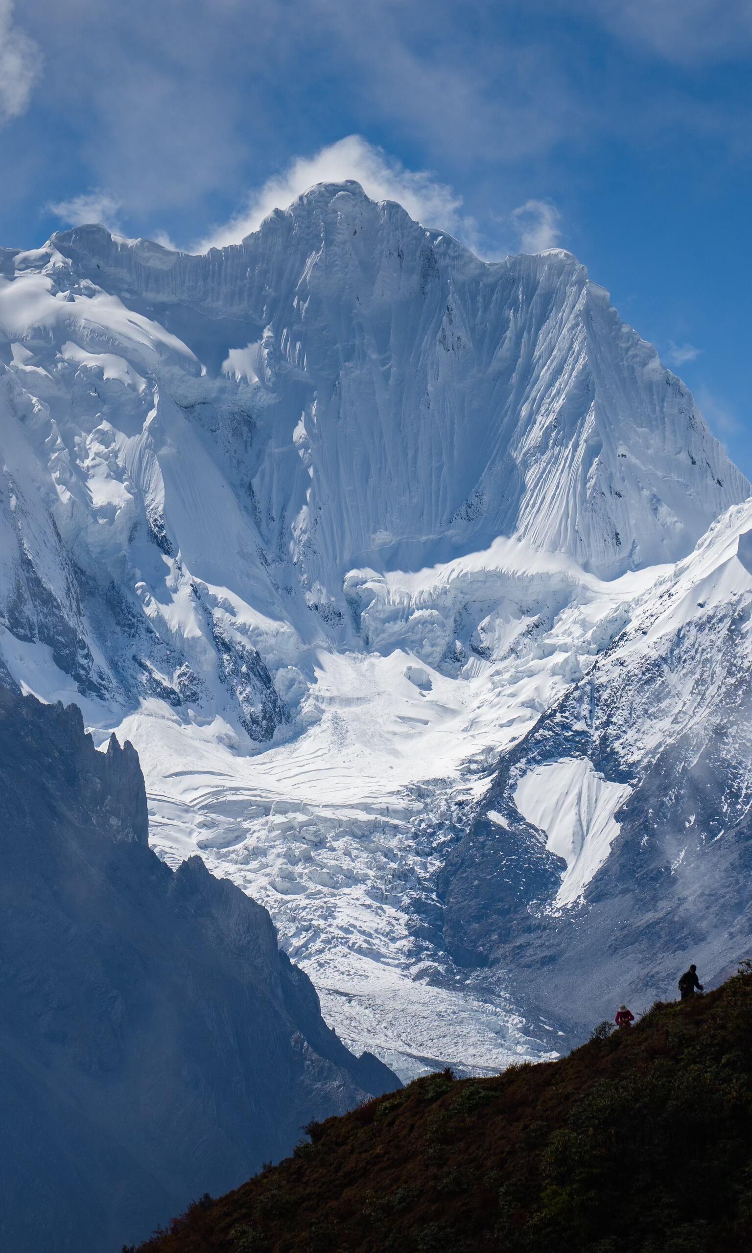 Massive snow peak looming over tiny trekkers — pure 'Land of the Gods' energy on Day 6