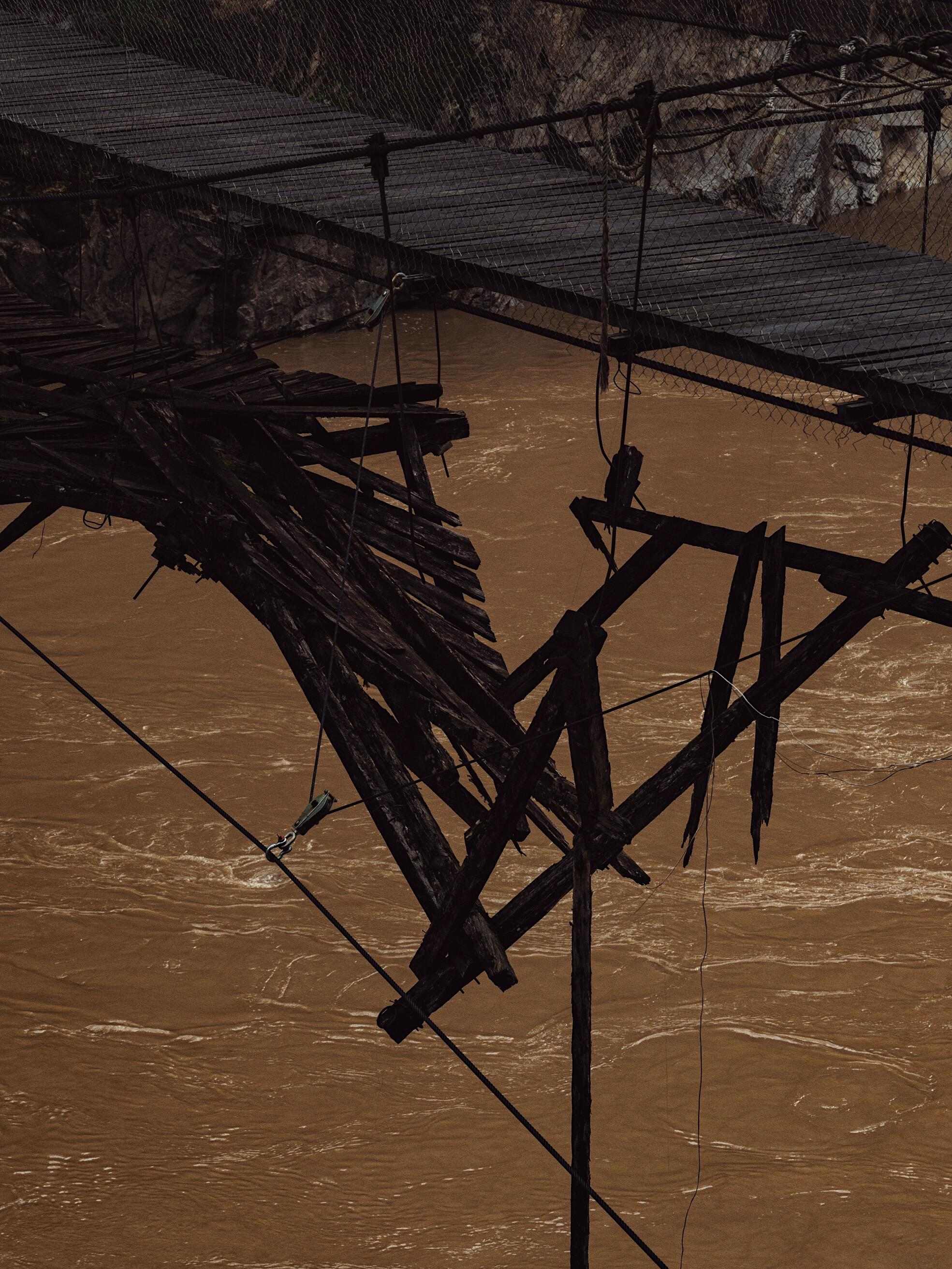 A broken, abandoned wooden suspension bridge dangling above the Salween River