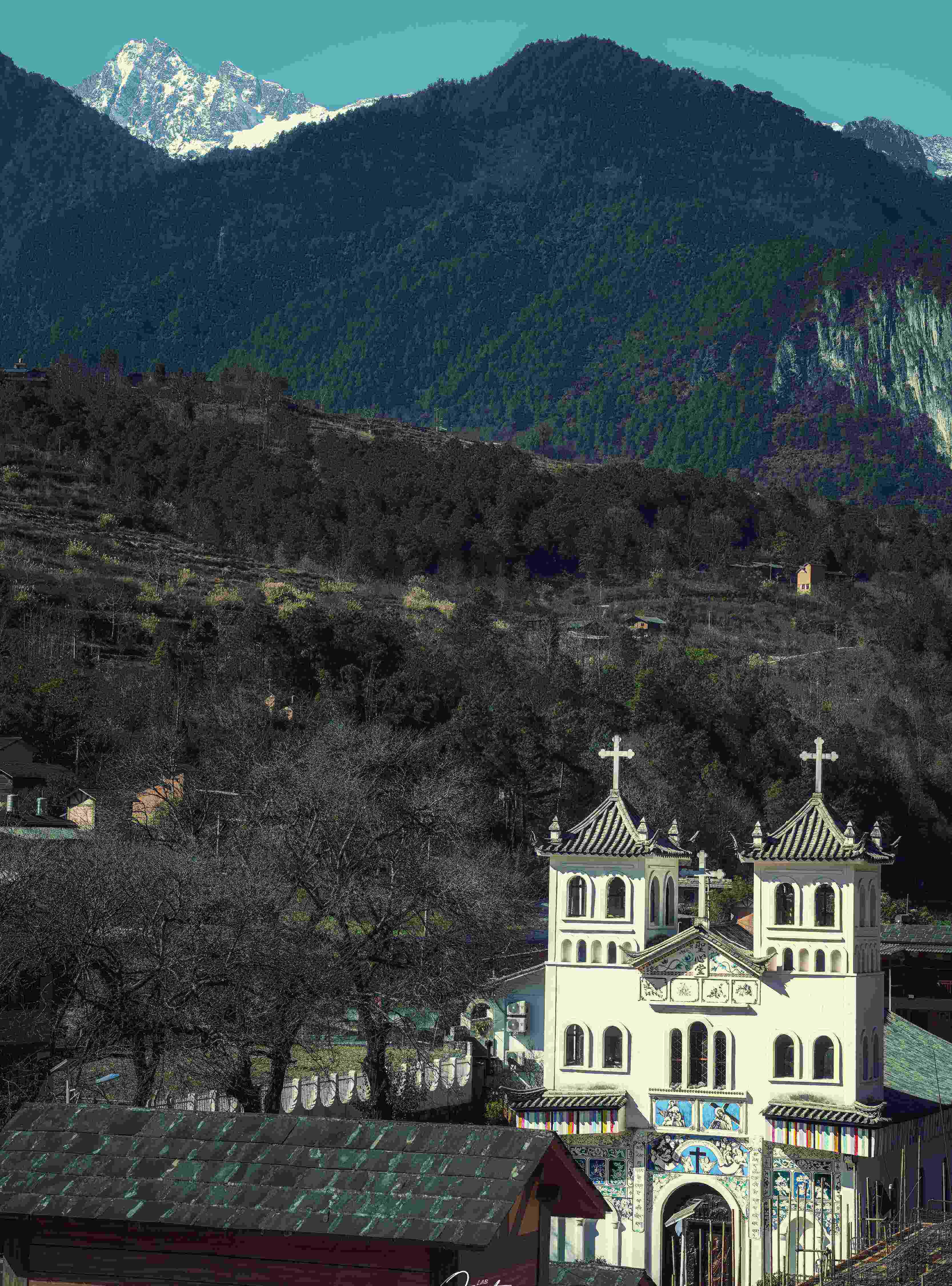 White twin-spire Catholic church under a Nujiang snow peak — a French-missionary legacy