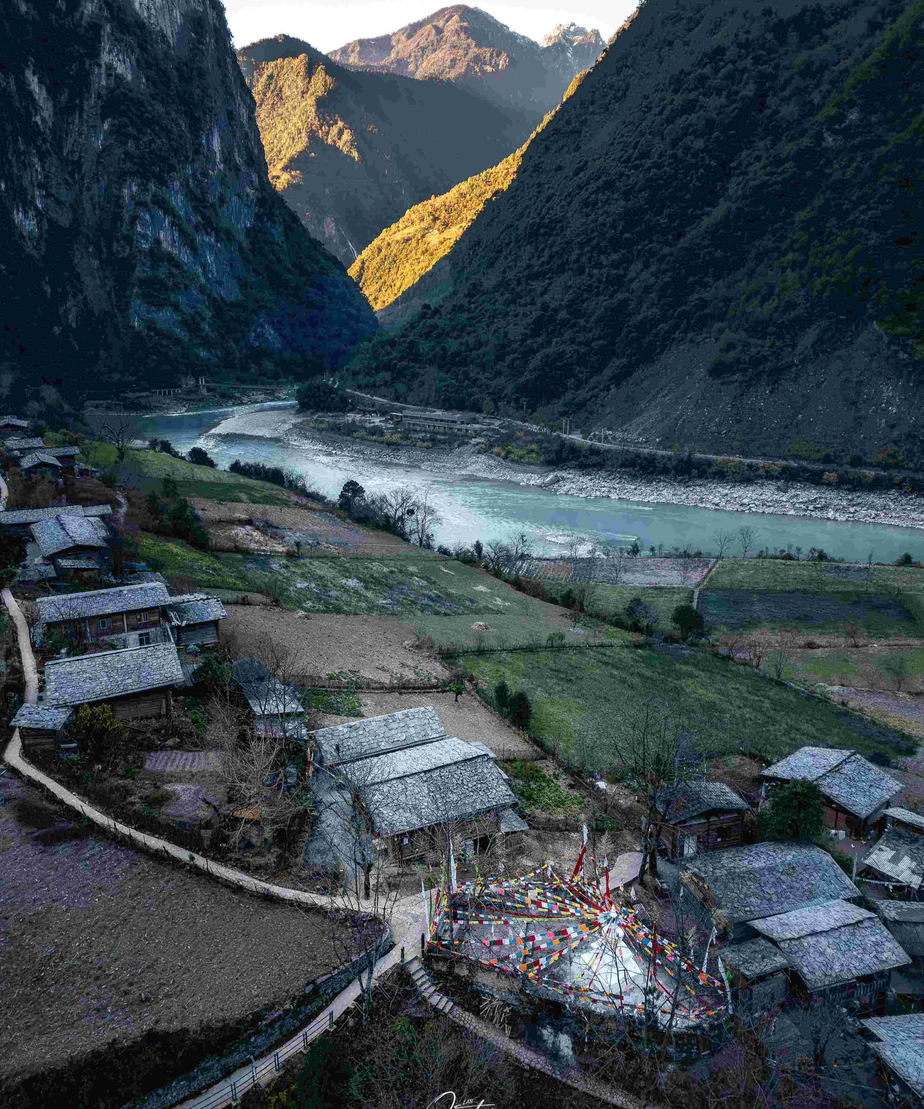 Stone-roofed Nujiang village at dawn with prayer flags above the turquoise Salween