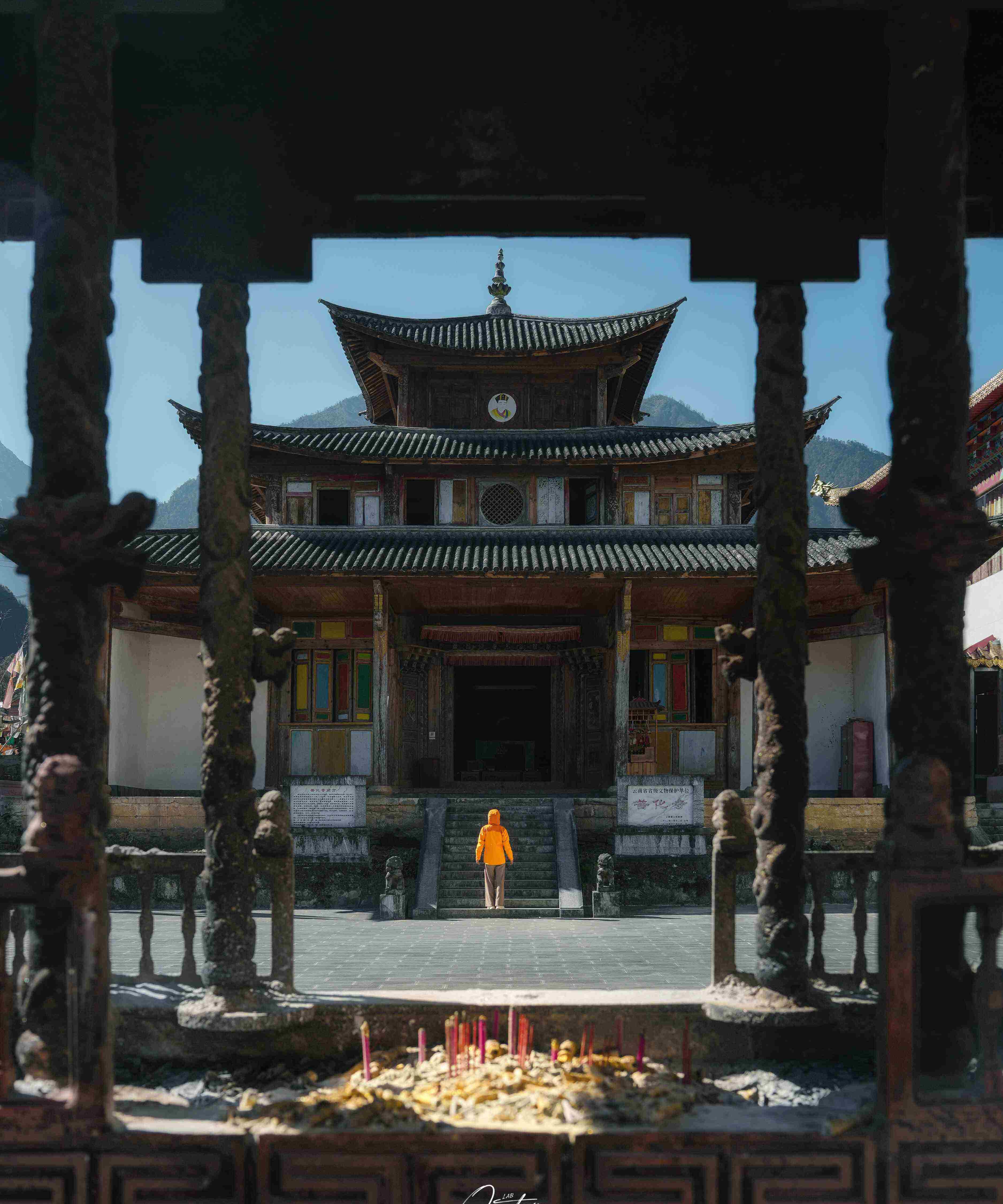 Nujiang temple courtyard — stone guardian lions, incense smoke, a monk walking up the steps