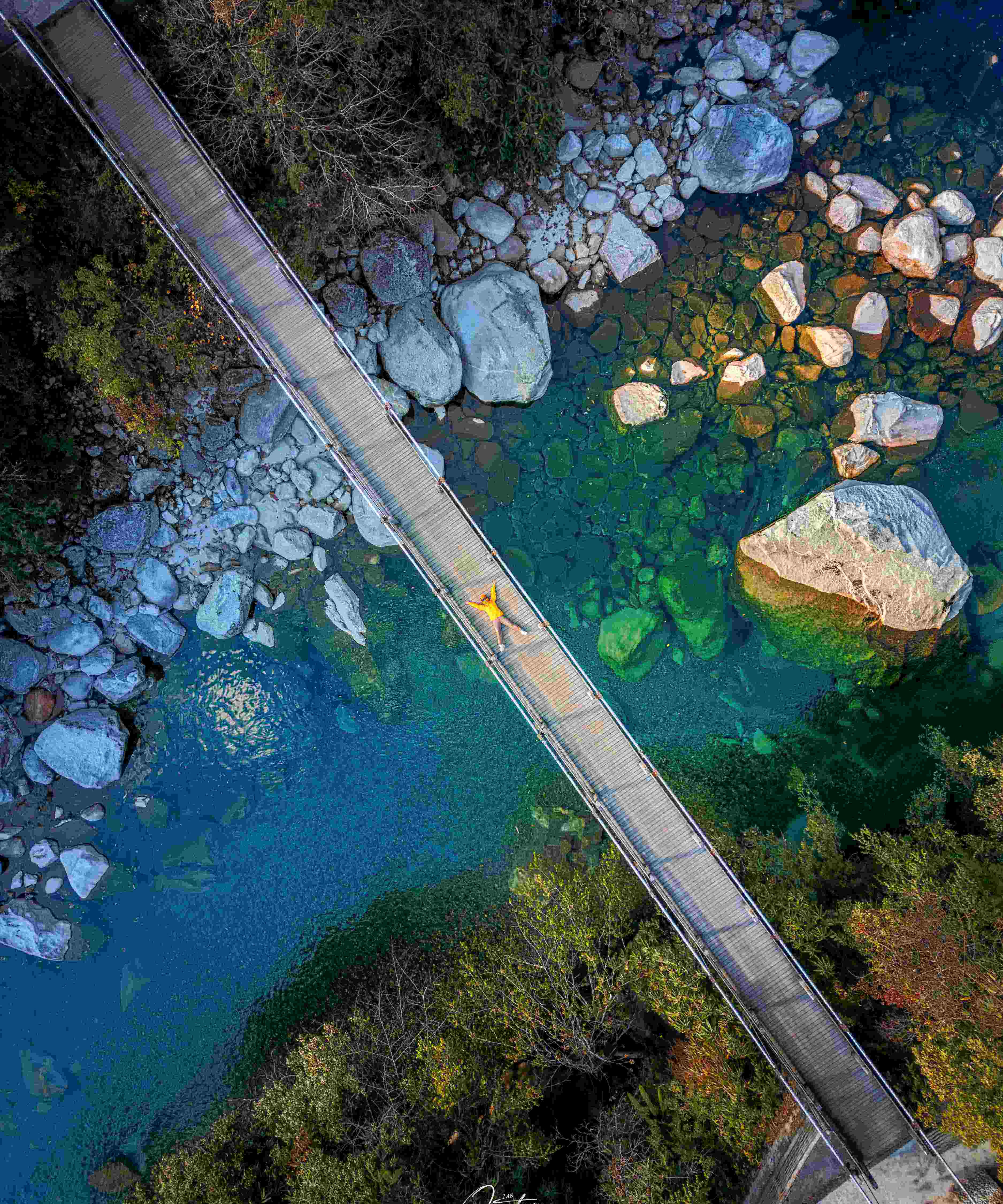Lone figure in yellow on a wooden footbridge over a gin-clear turquoise Nujiang creek