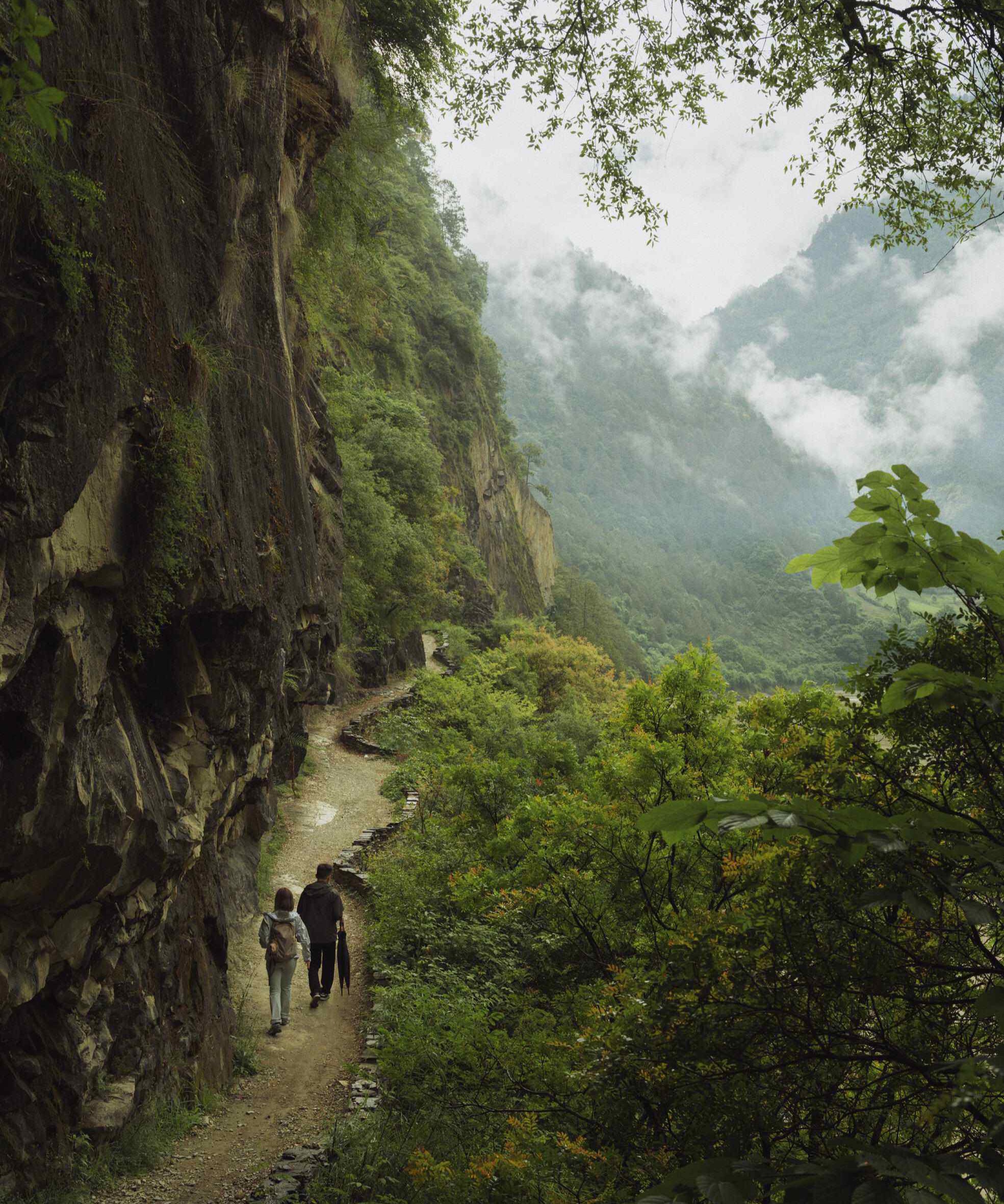 Two hikers on the 1,800m Wuli Tea Horse Road — ancient trail carved into a Nujiang cliff face