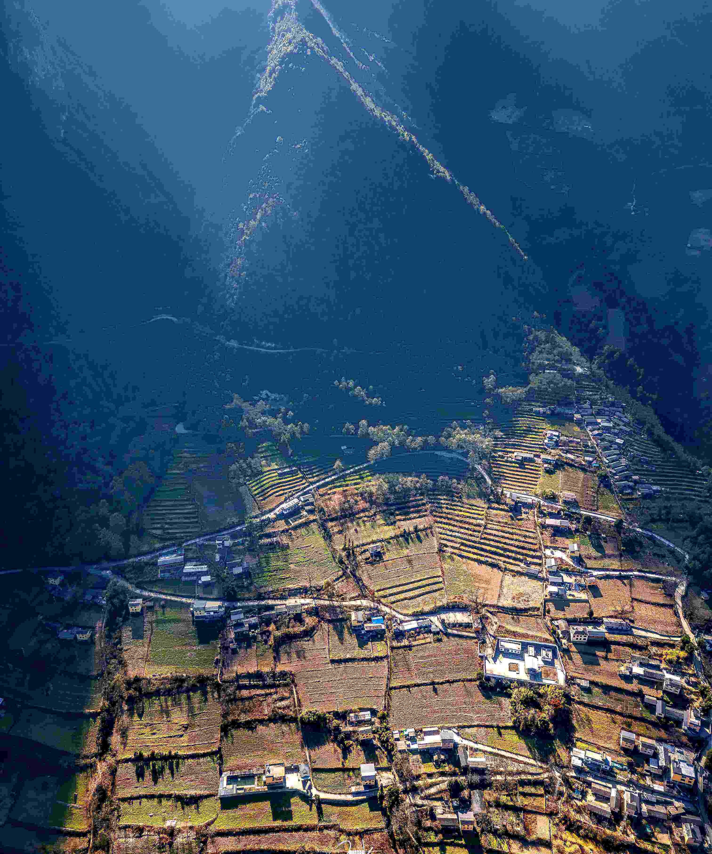 Aerial of a ridge-back village wreathed by terraced fields catching slanted evening sun