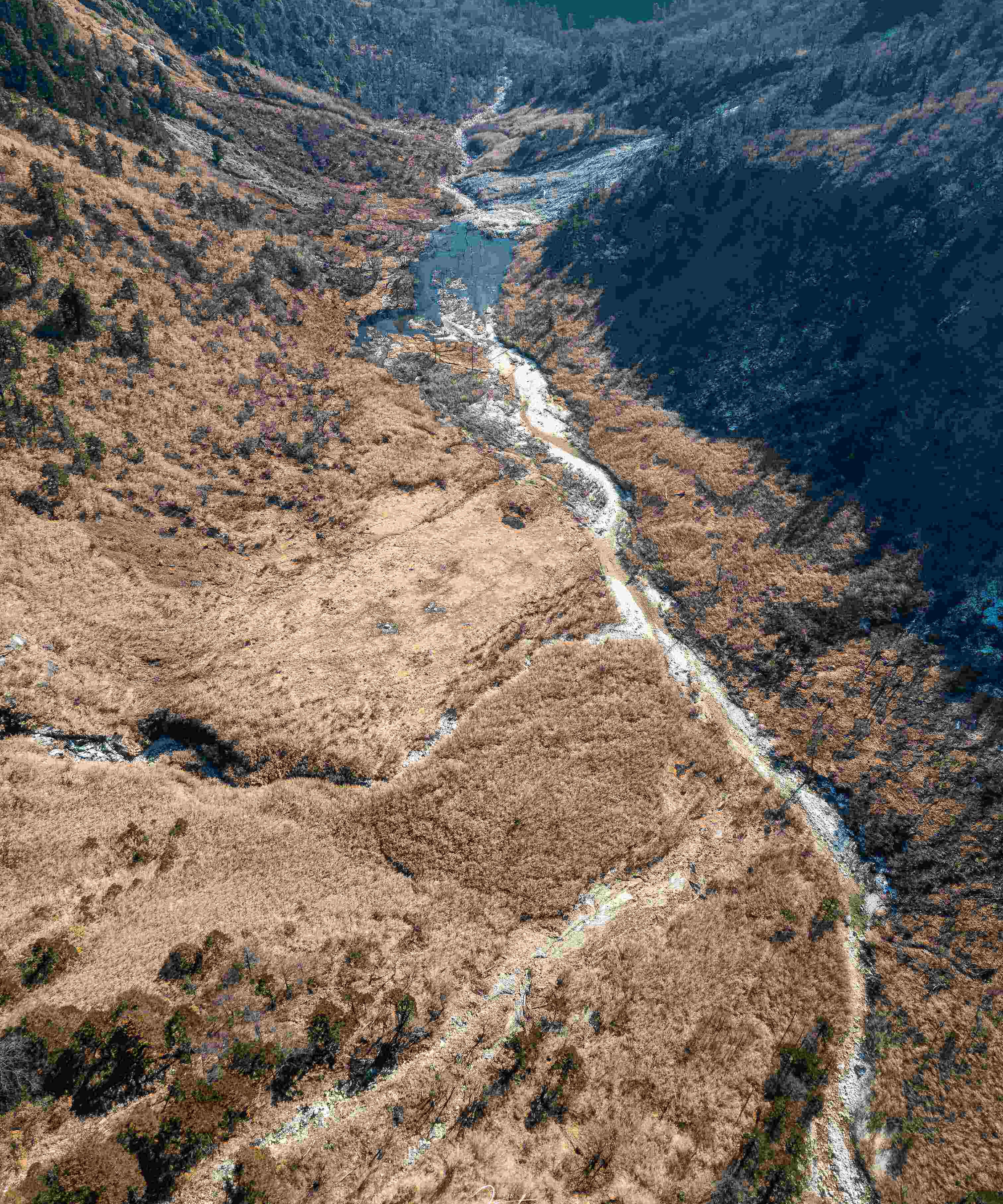 Braided meltwater stream winding down a snow-dusted high valley above Nujiang