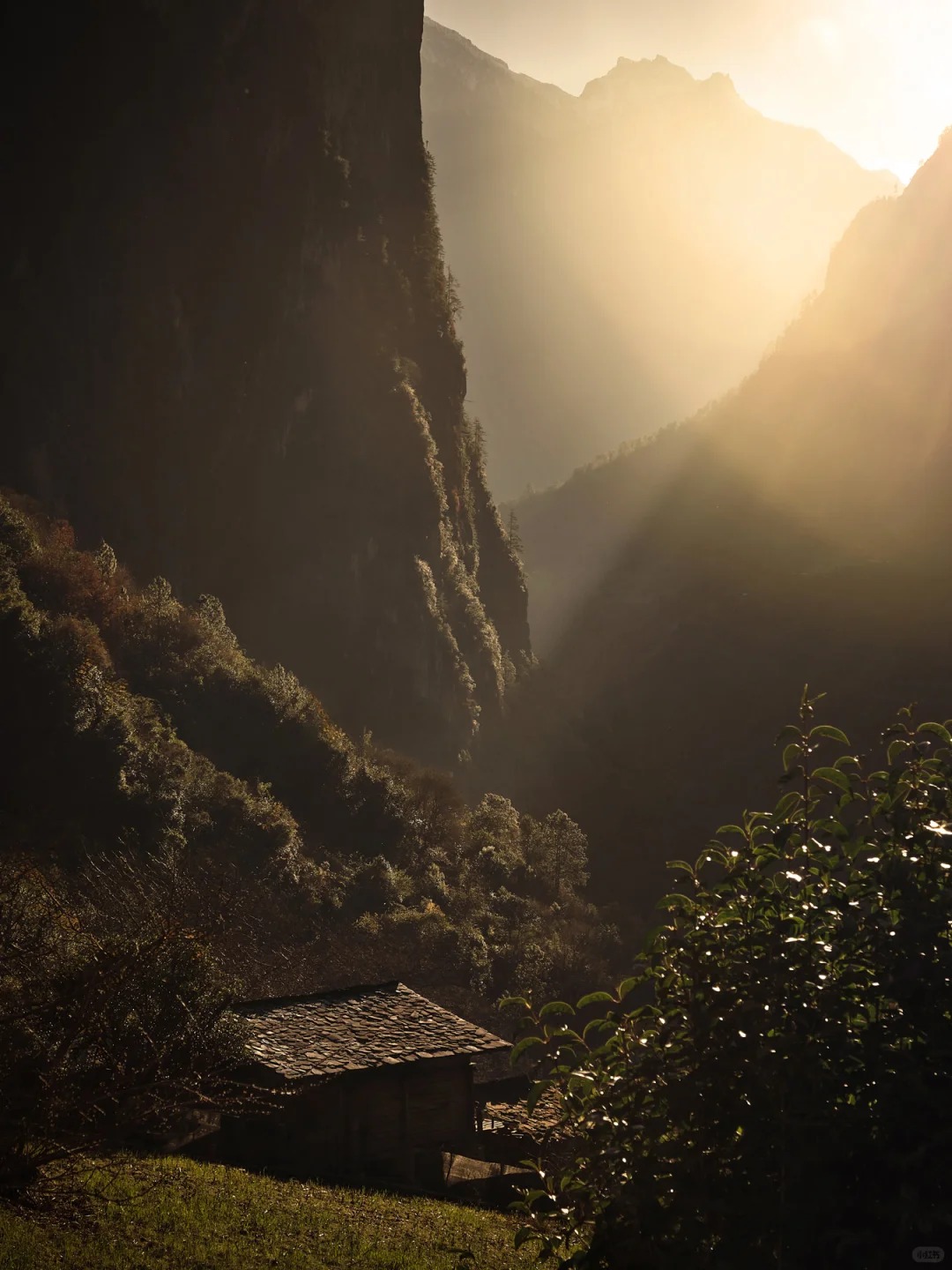 Late-afternoon sun streams between Nujiang canyon walls past a solitary stone farmhouse