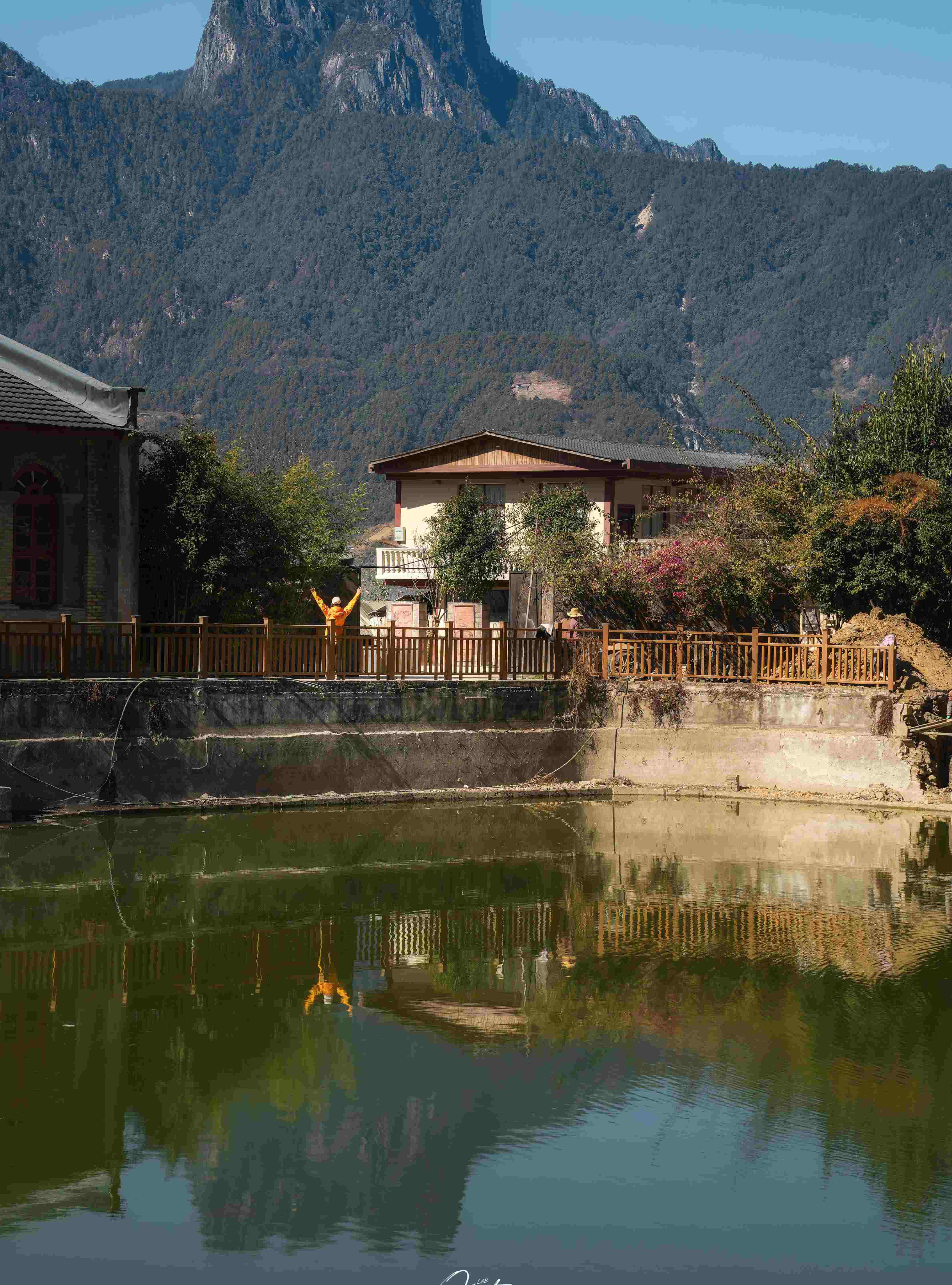 Traditional house mirrored in a village pond with Stone Moon Peak rising behind