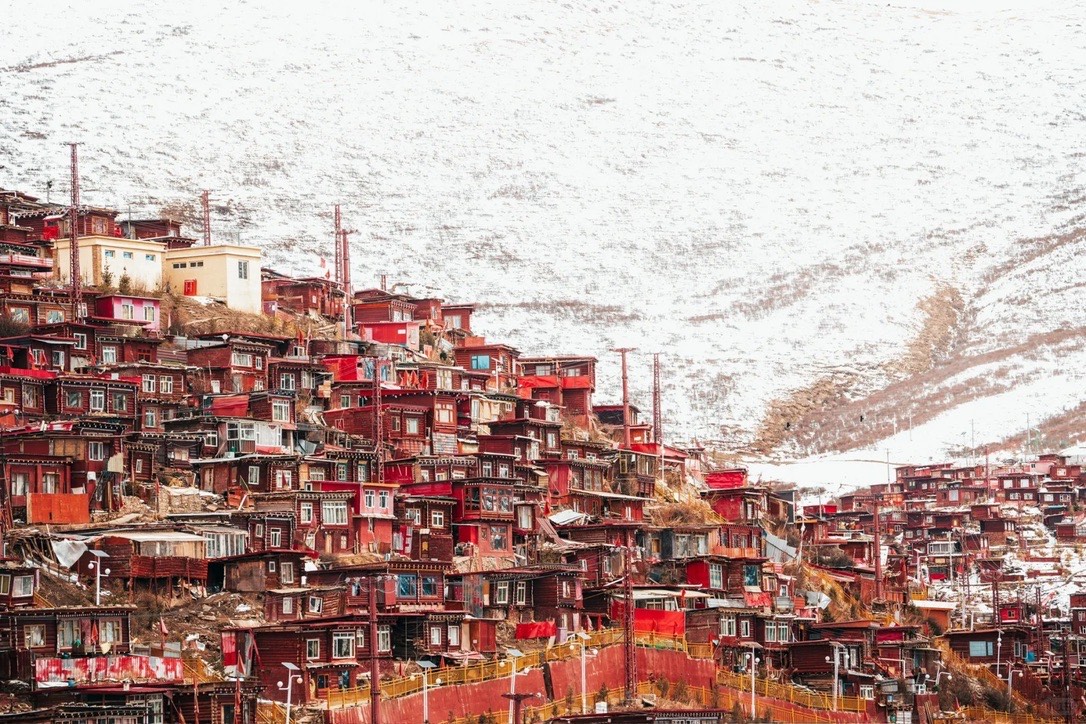 Terraced red timber dwellings of Seda packed across a hillside below a vast snow-covered mountain slope.