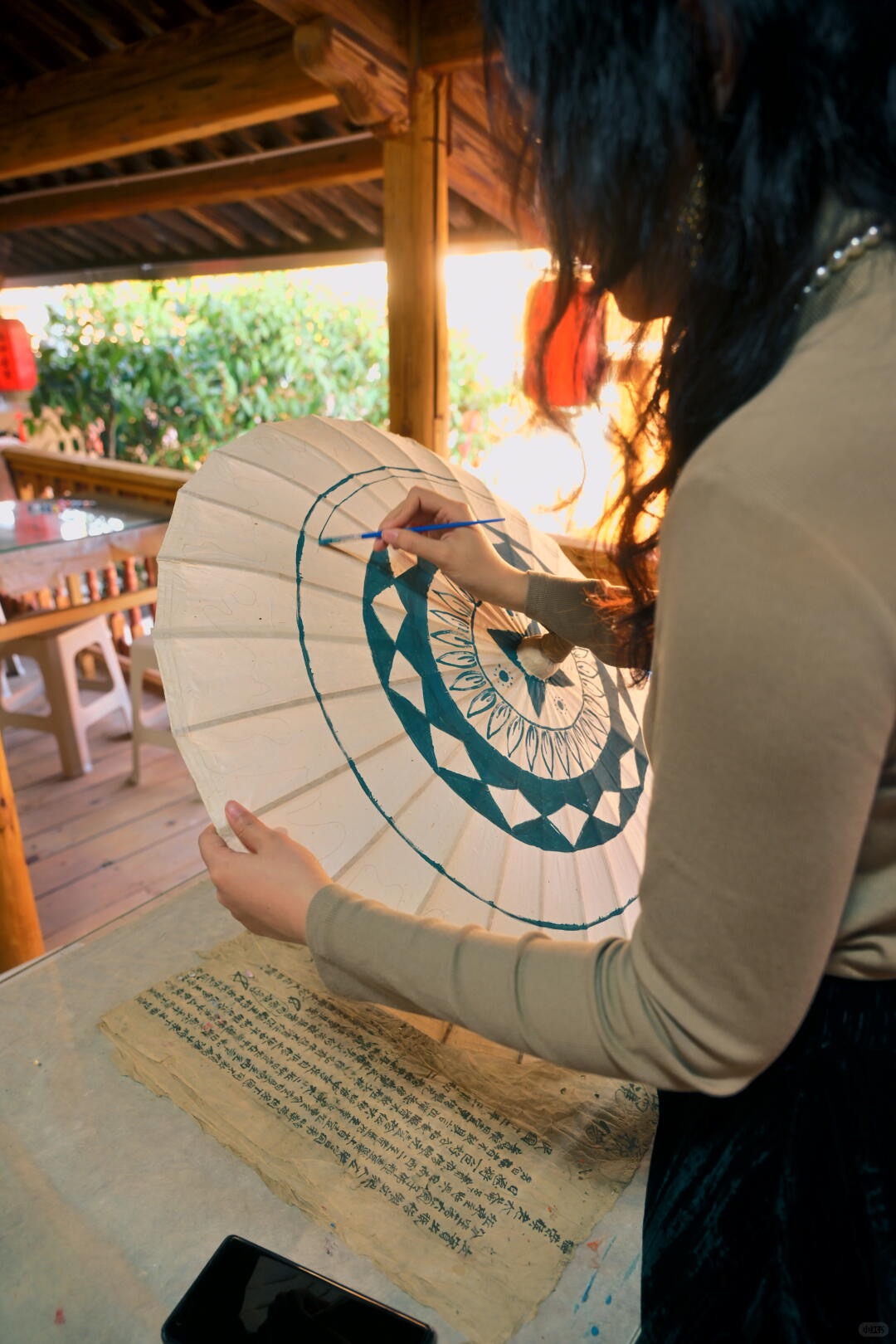 Young guest hand-painting an indigo pattern onto a Heshun oil-paper umbrella in a craft workshop