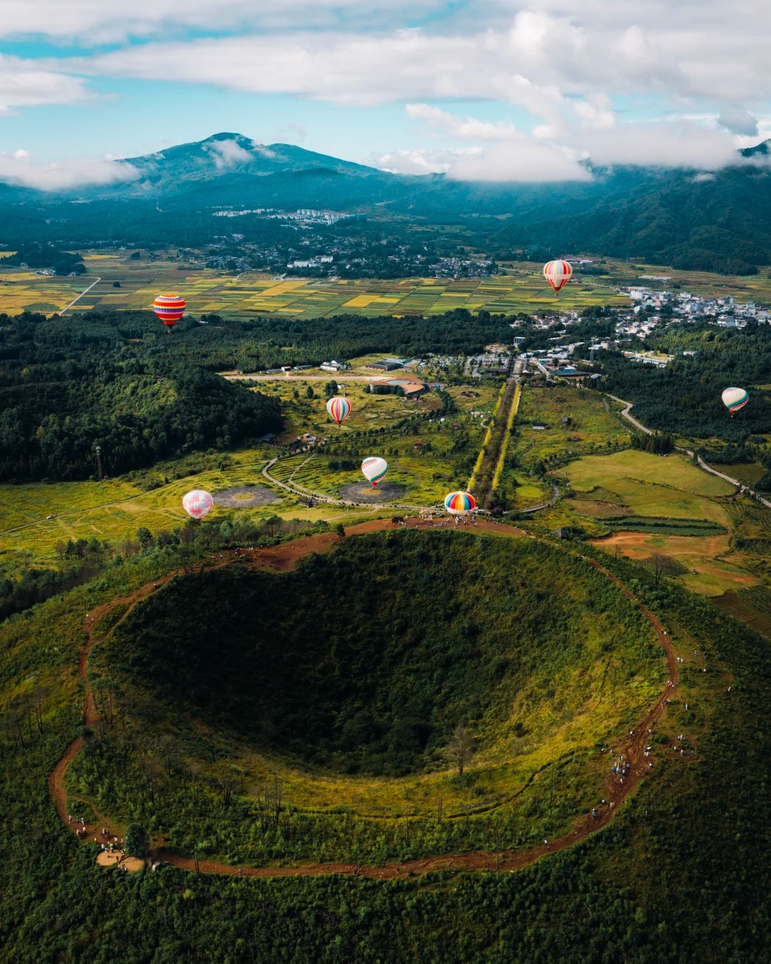 Hot-air balloons drifting over a grassy volcanic crater, Tengchong
