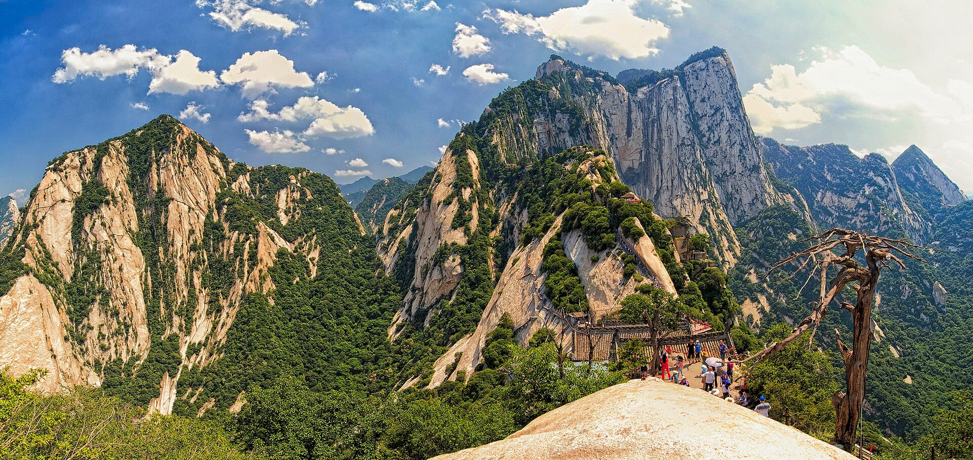 Granite peaks and pine-covered ridges of Huashan under a blue sky, walkers on a summit path