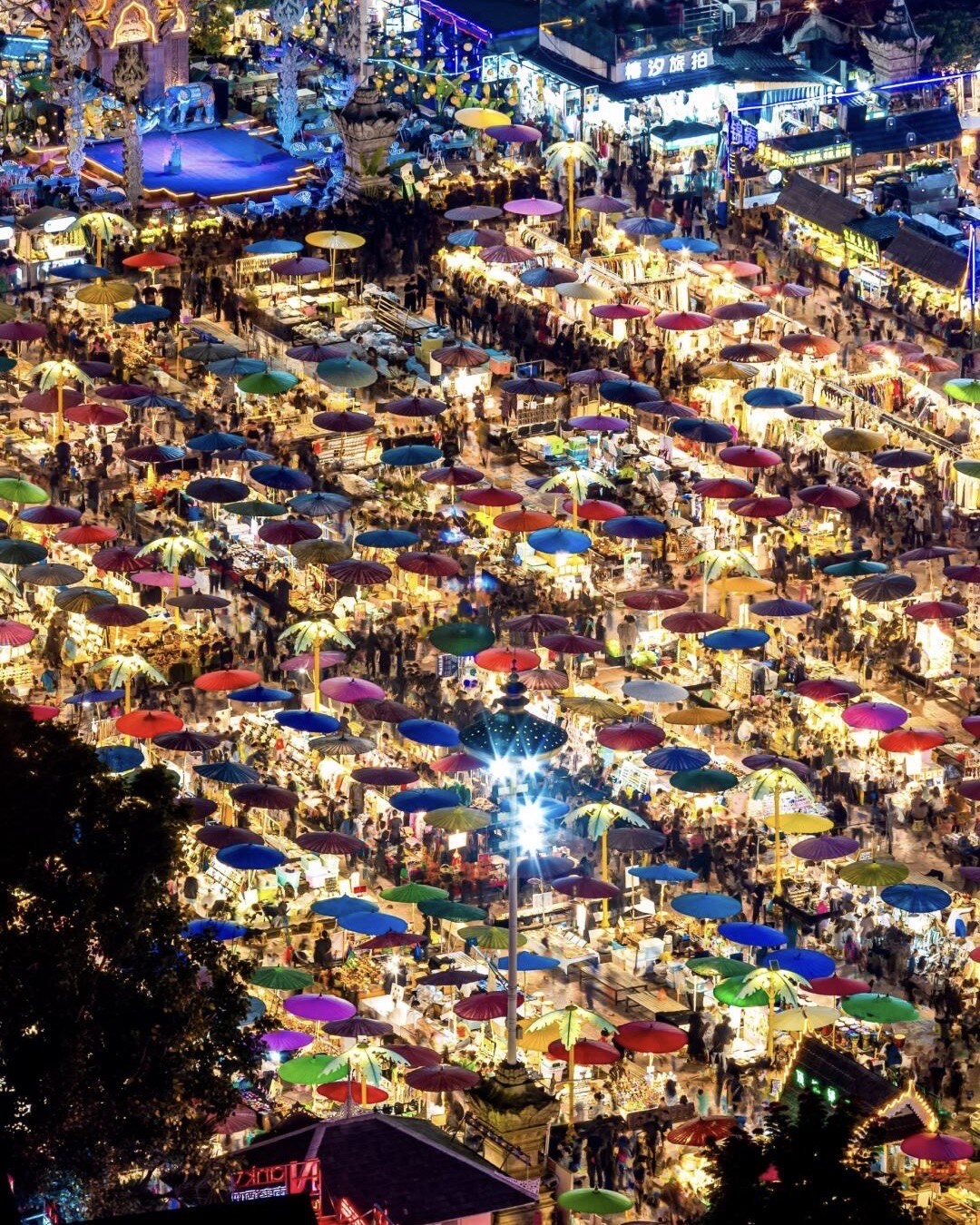 Aerial view of a night market packed with rows of brightly coloured parasols and glowing stalls.