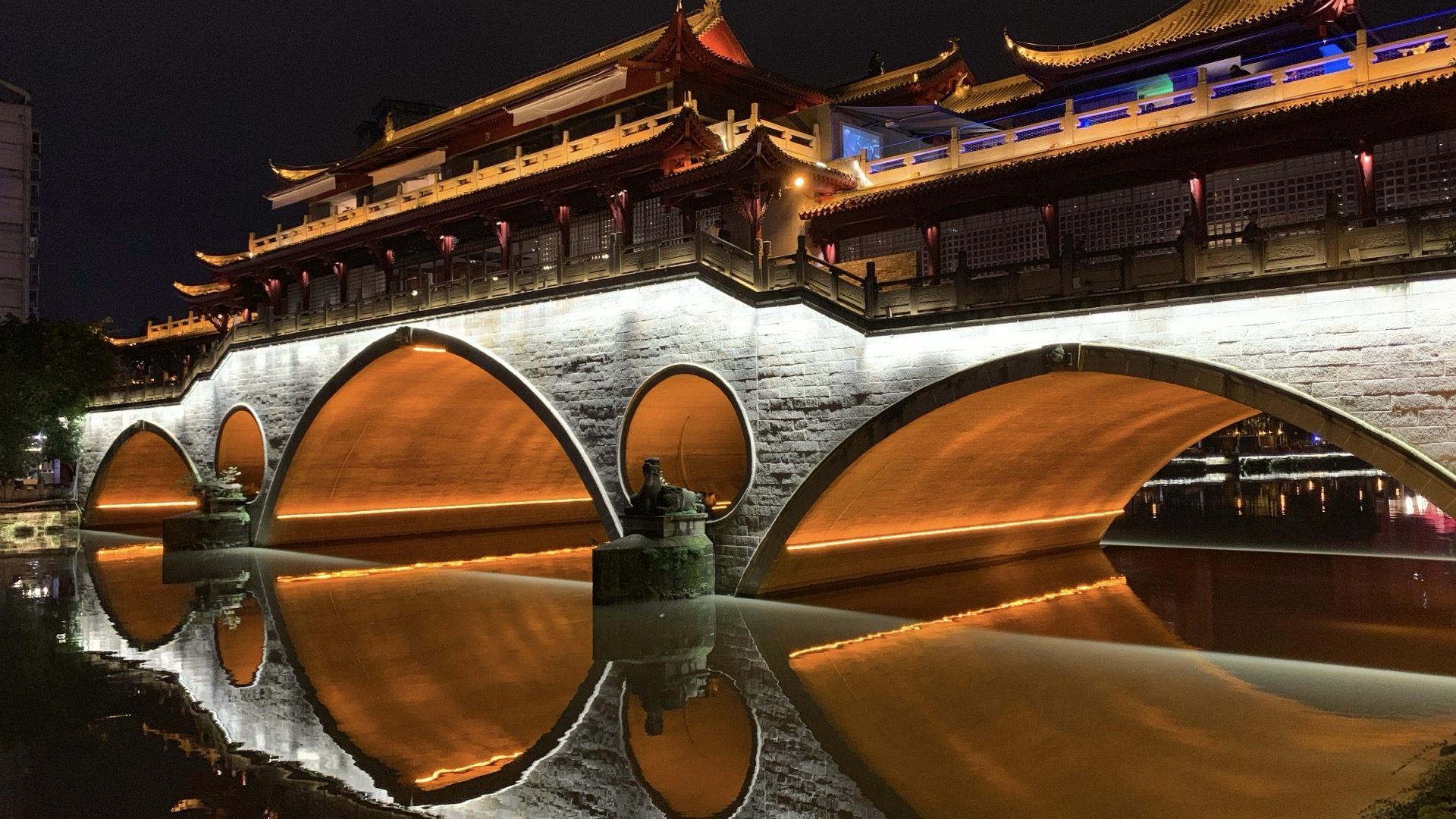 Illuminated stone arches of Chengdu's Anshun Bridge reflected in the Jin River at night