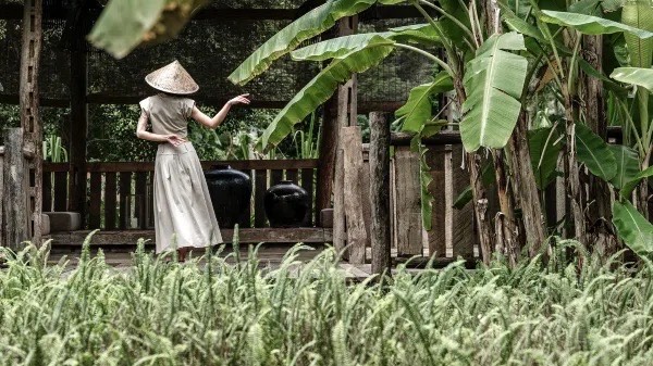 Traveller in a bamboo hat in a heritage Yangshuo courtyard framed by banana palms — hero image for a private Guilin tour by Boutique China