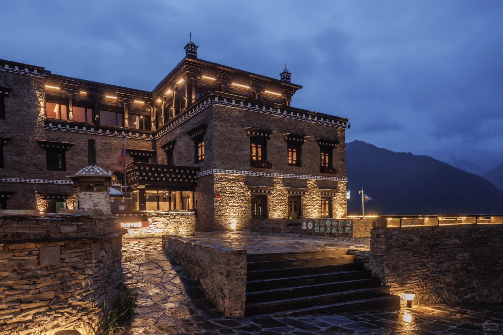 A Tibetan-style stone lodge lit at dusk in the Daocheng Yading valley — final night before the fly-out