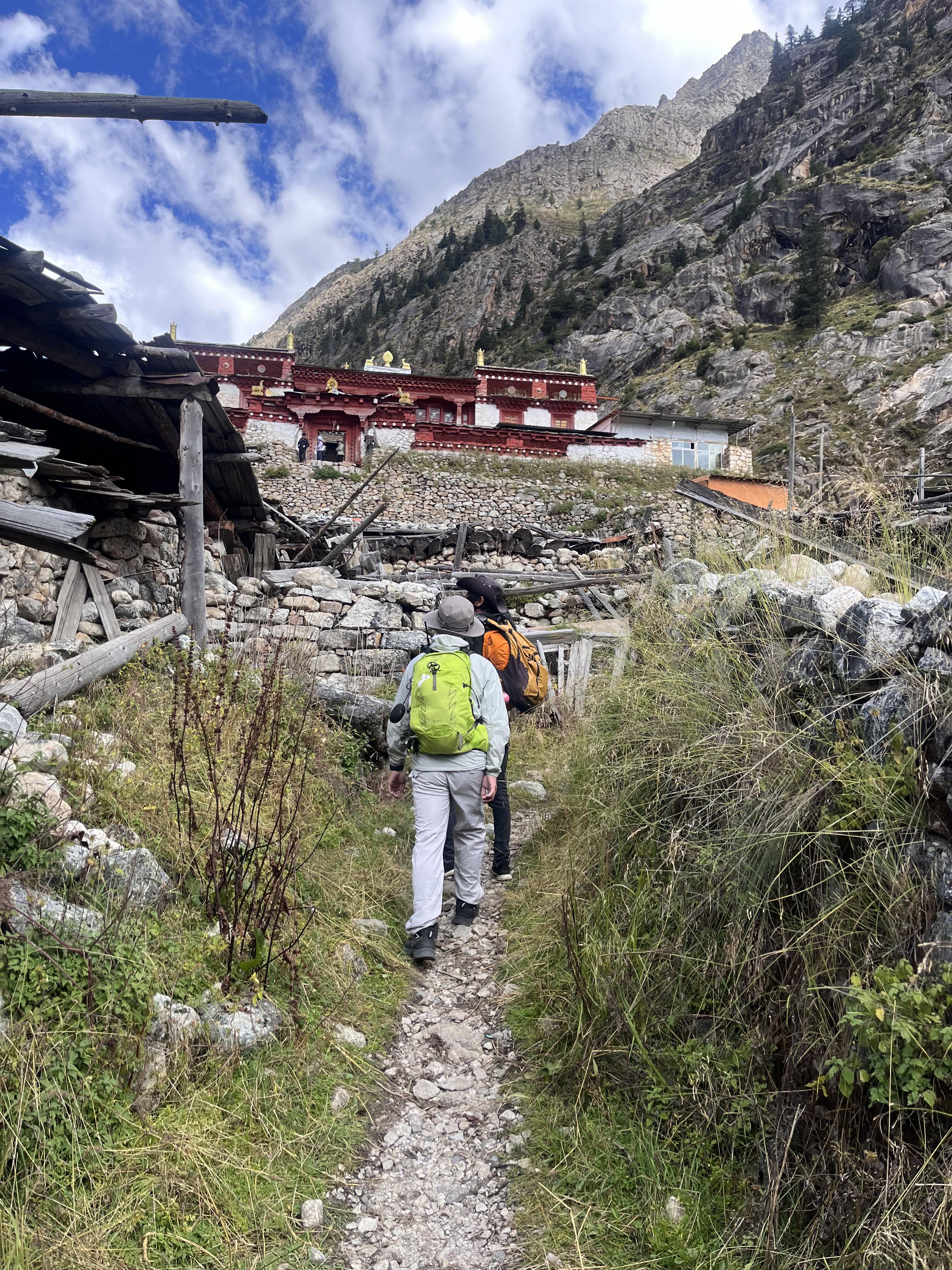 Trekkers approaching Leng-Gu Temple up the stone-walled trail below Mt Genie's jagged ridge