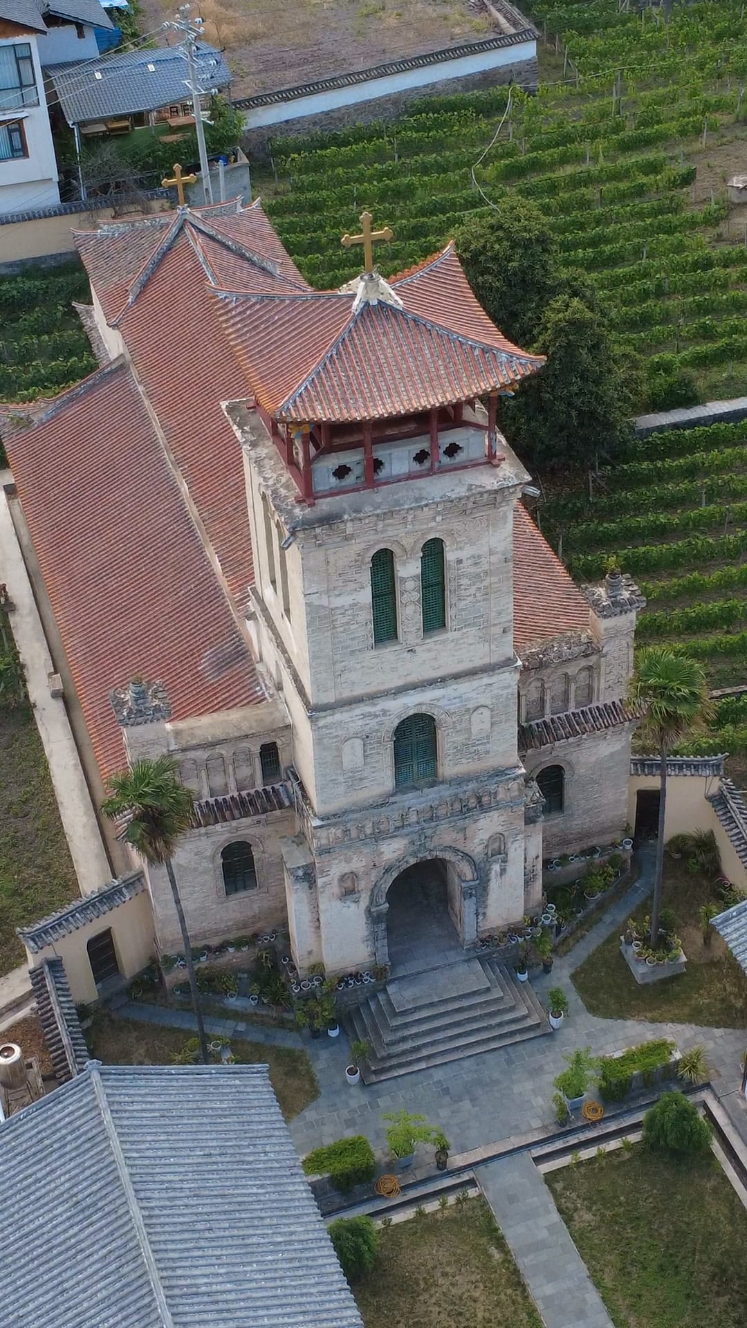 The Cizhong Catholic church (茨中天主教堂) from above, its bell tower rising beside rows of vines — Shangri-La Wine Journey