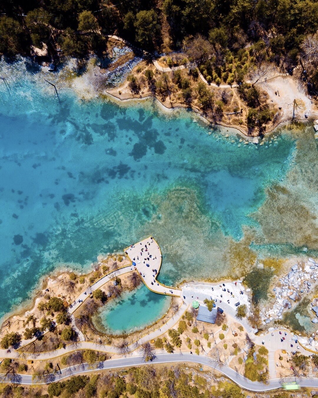 Aerial view of a wooden boardwalk winding through a turquoise alpine lake in Sichuan's highlands