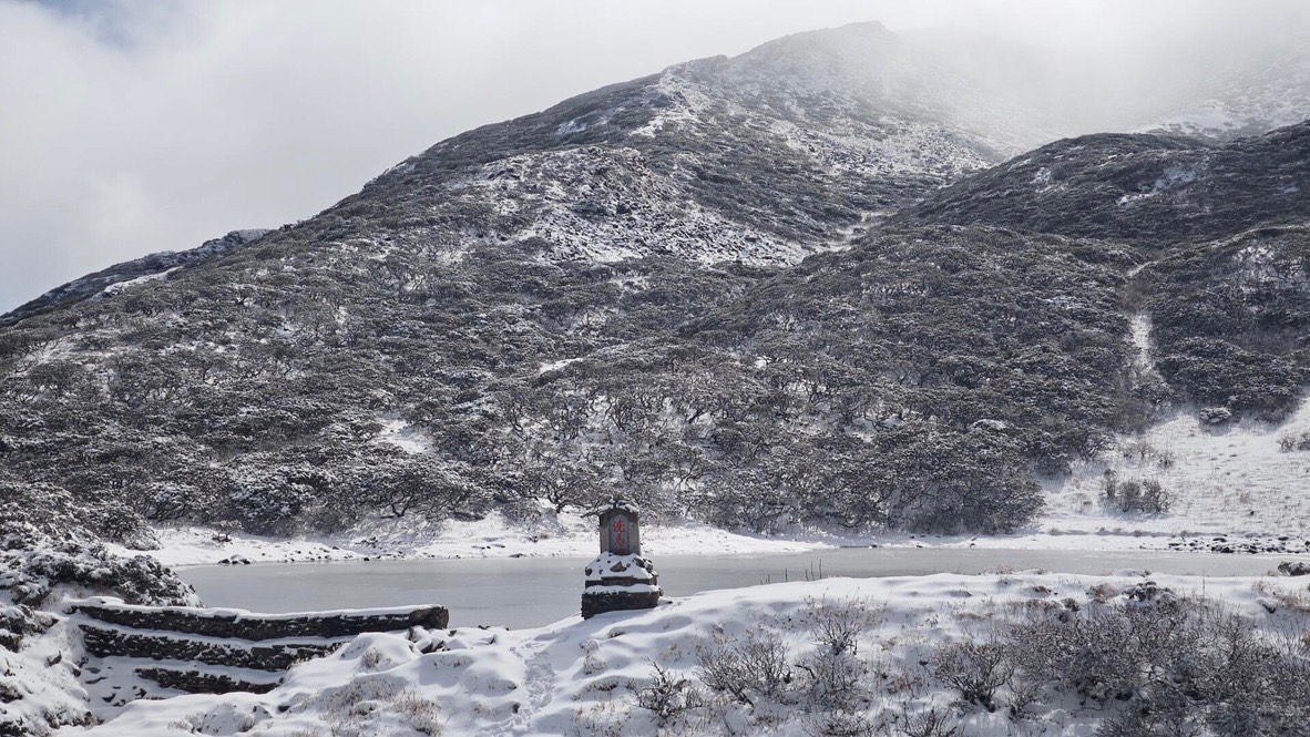 Snow-covered Cang Mountain slopes above a small frozen alpine lake and shrine