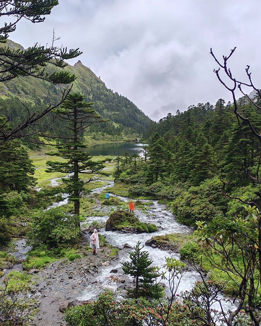 Hikers crossing a stream in Yubeng's alpine meadow on a Meili Snow Mountain trek