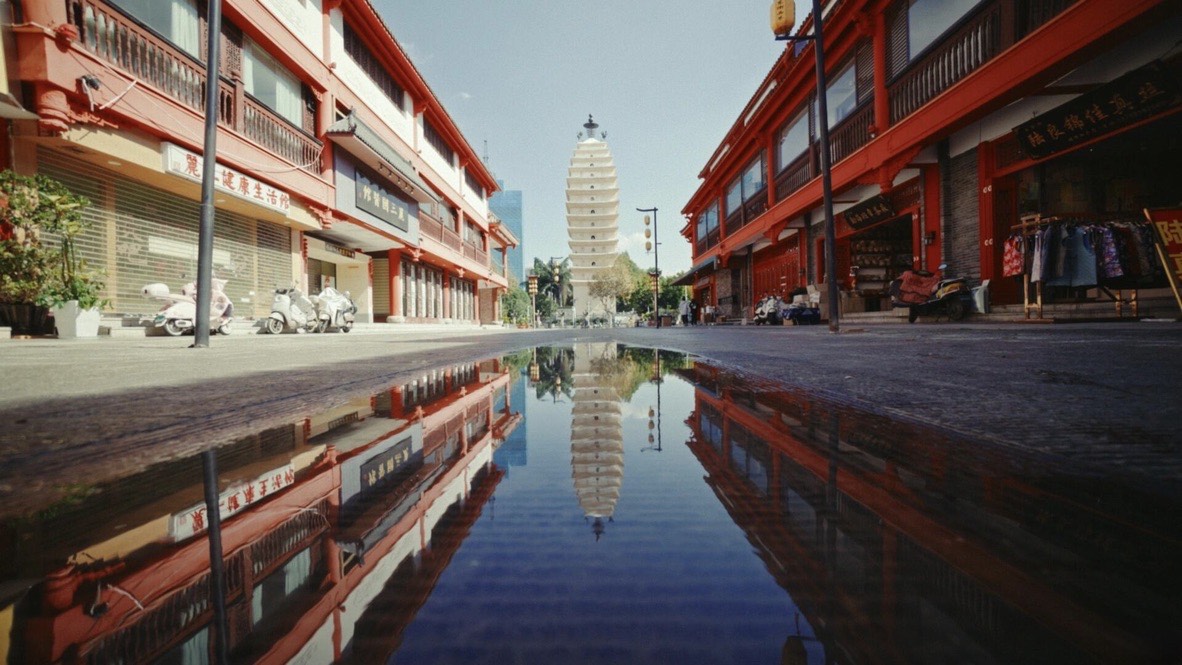 Kunming's East and West Pagodas reflected in a rain puddle on a quiet city street — Yunnan slow culture tour